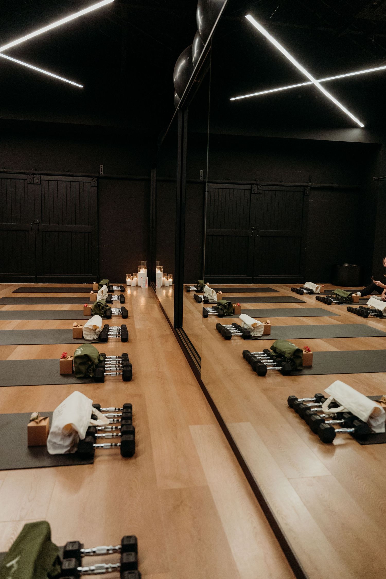 Modern yoga studio with gray mats, dumbbells, and candles arranged on hardwood floors under sleek LED lighting.