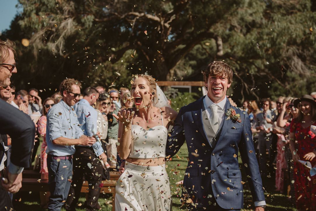Wedding celebration with confetti toss outdoors among joyful guests.