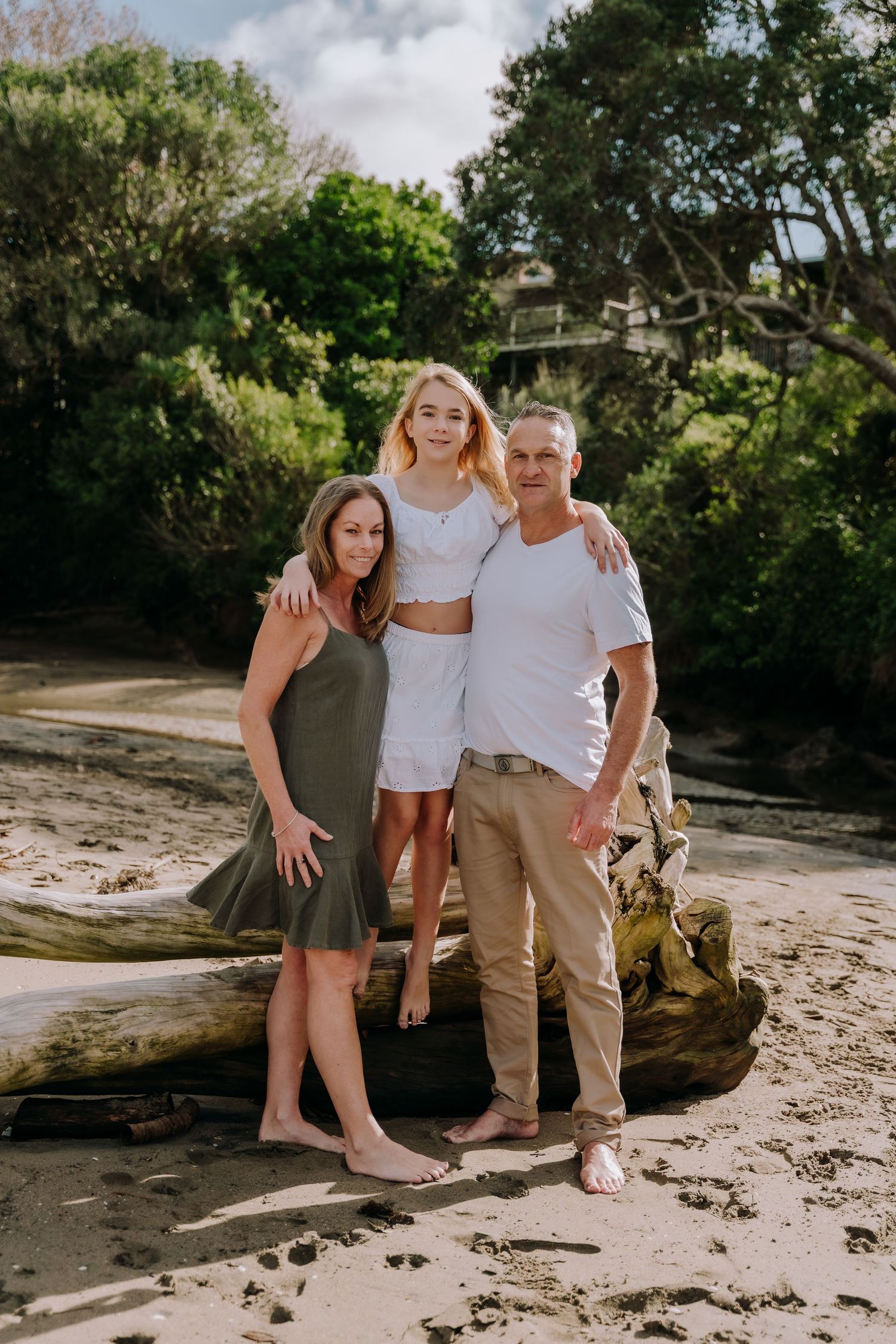 A family enjoys quality time together on a rocky beach surrounded by lush greenery on a sunny day.