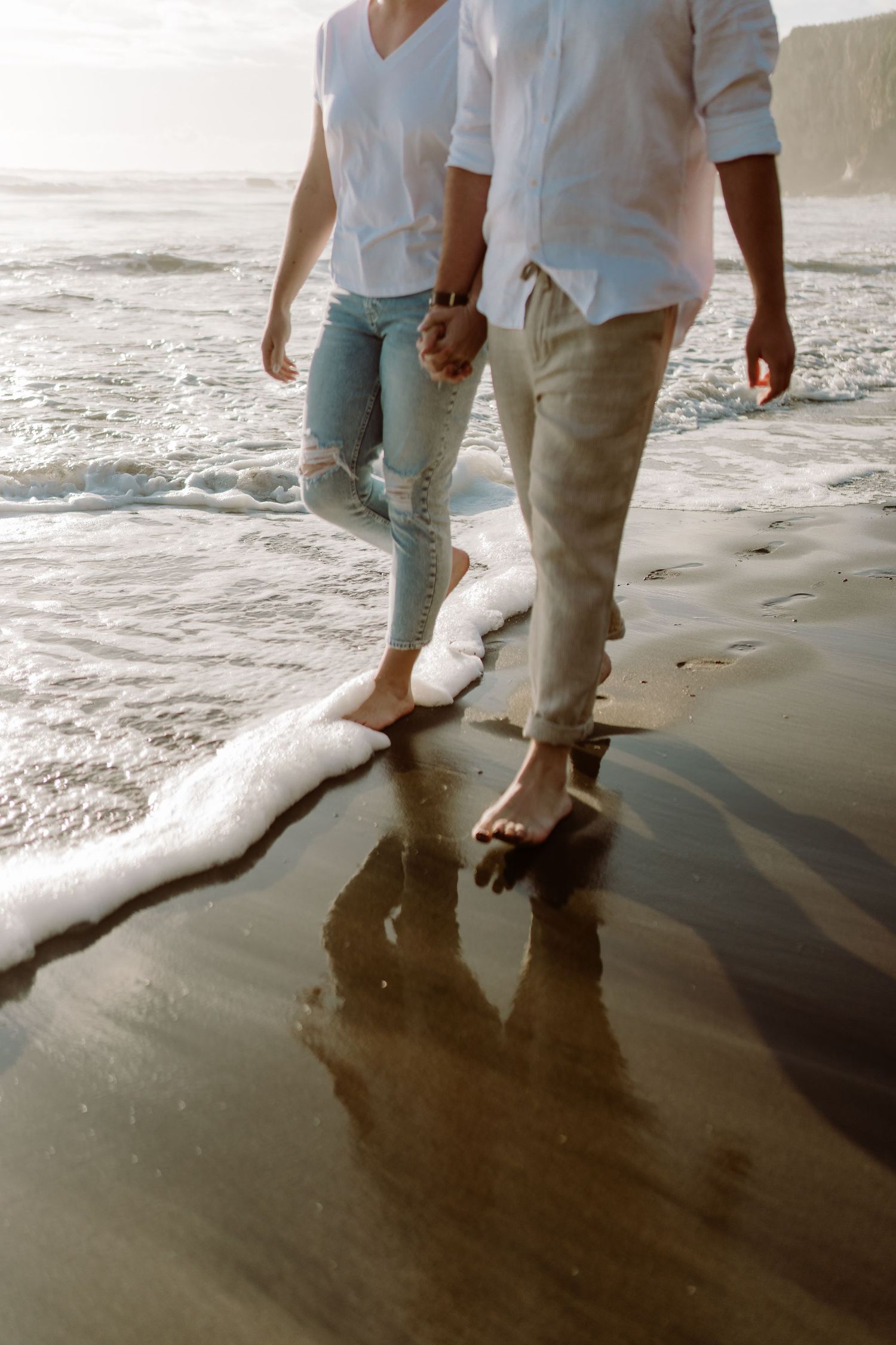 Two pairs of legs walking on wet sand at the ocean's edge during golden hour.