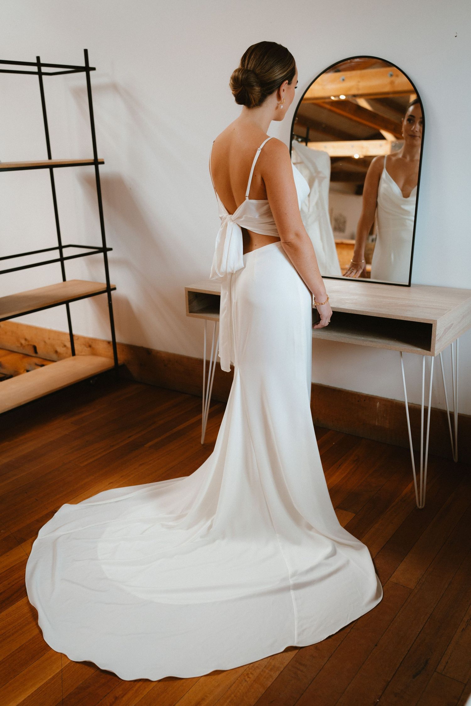 Modern wedding dress with open back detail and flowing train in minimalist setting.