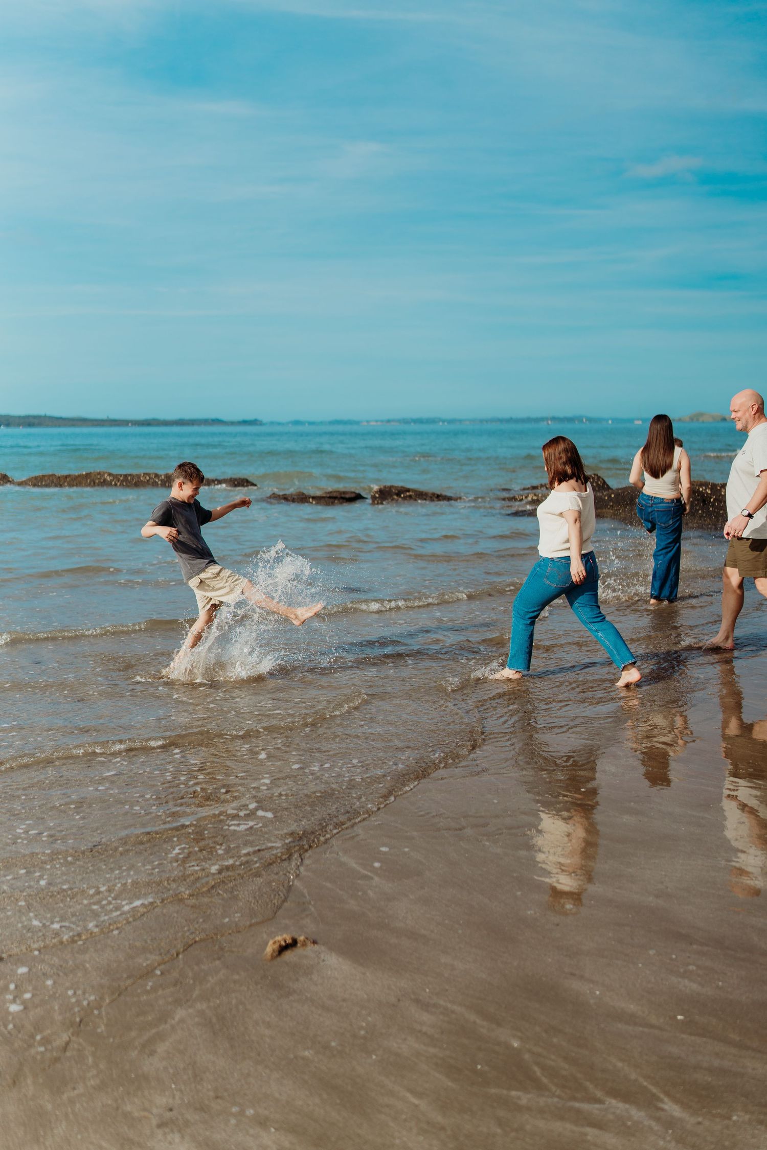 Family playing in ocean waves on a sandy beach on a sunny day with blue skies.