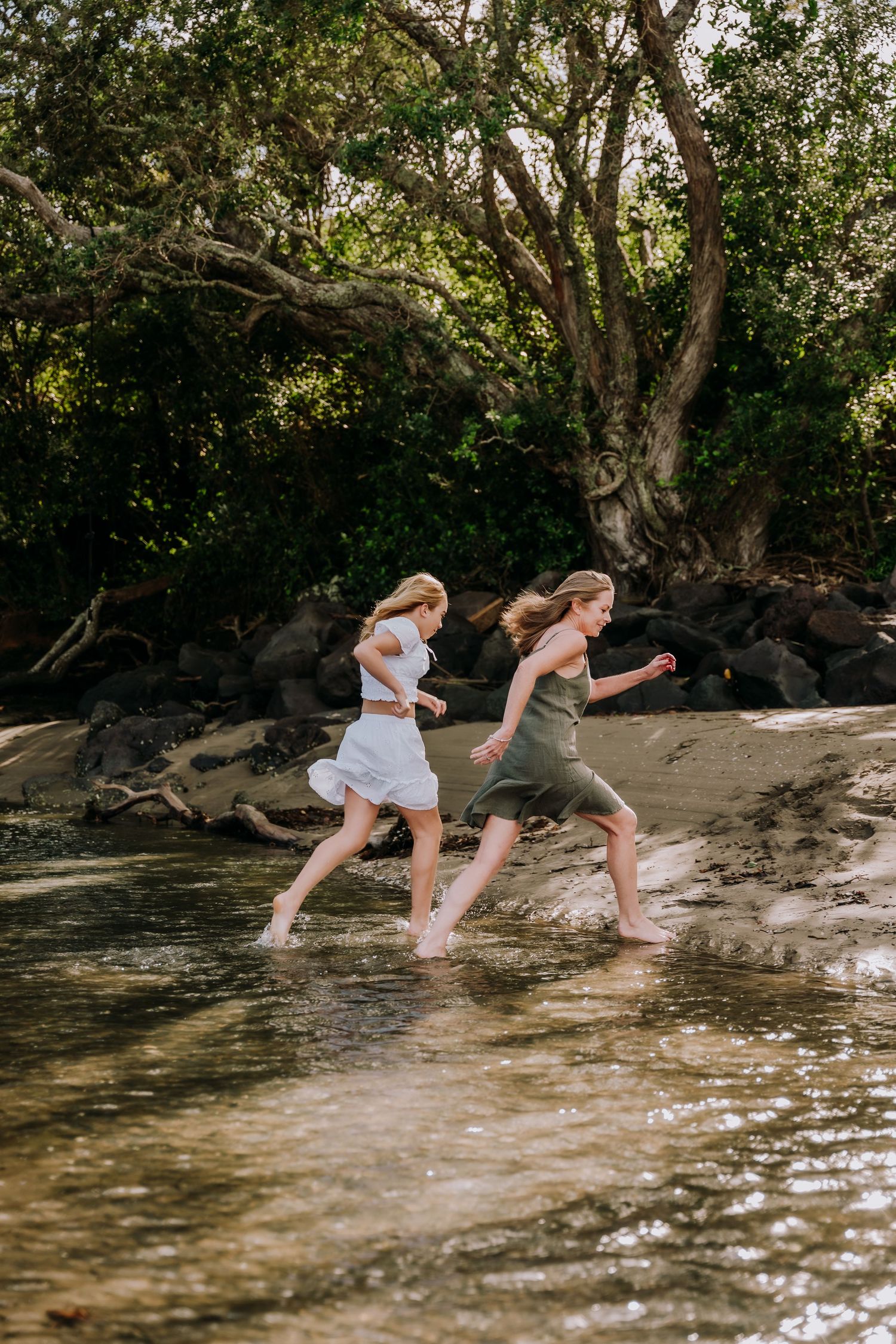 Two people in white dresses splash and play together in shallow creek water on a sunny summer day.