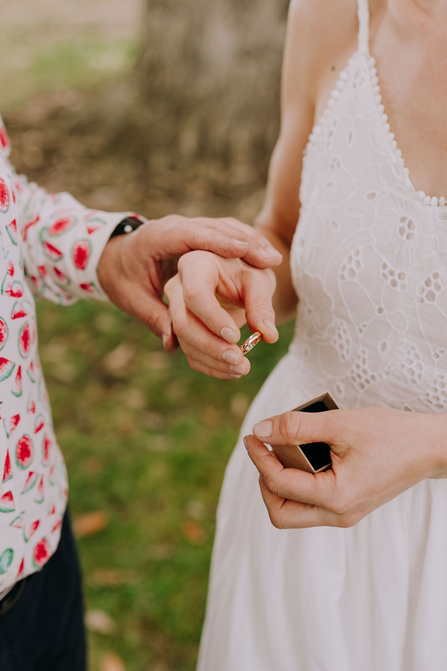 Close-up view of hands holding a small black ring box in a white lace dress.