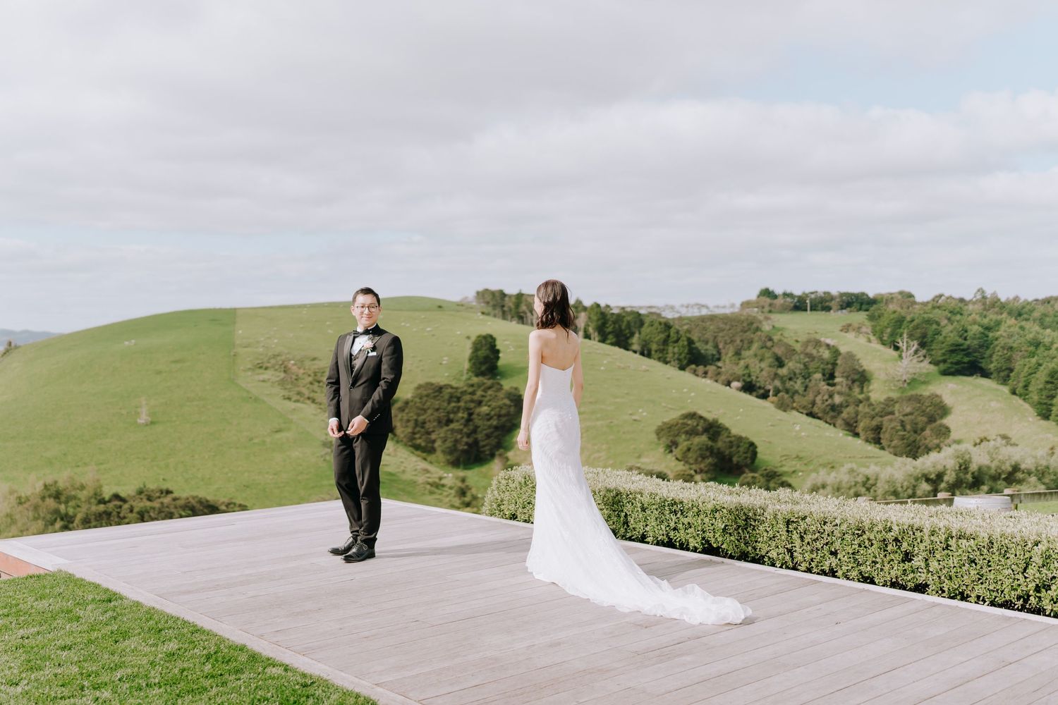 Wedding couple standing on wooden deck overlooking rolling green hills and countryside.