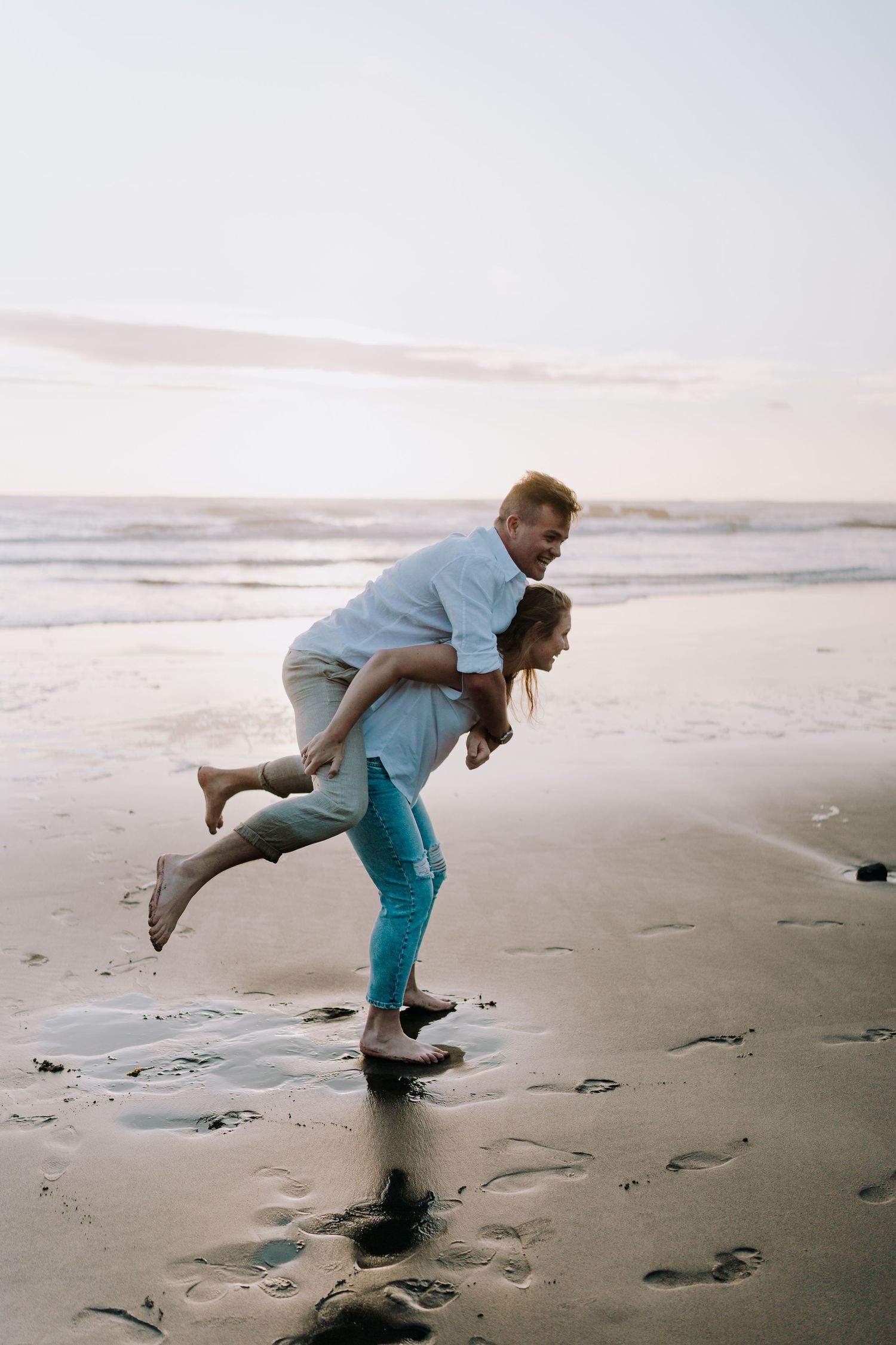 Playful couple having fun with piggyback rides on a sandy beach at dusk.