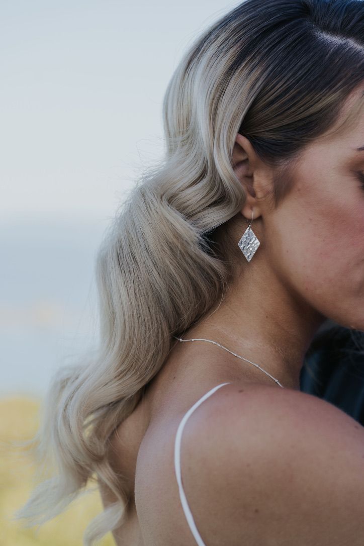Close-up view of a diamond stud earring on a person wearing a white spaghetti strap dress against a blurred background.