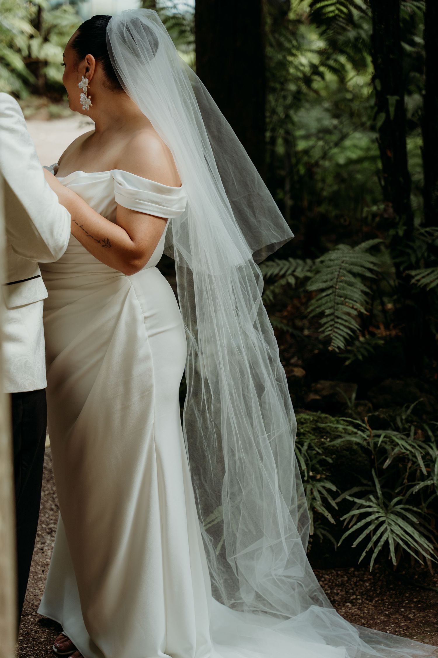 Elegant white wedding dress and veil details captured in a natural outdoor setting.