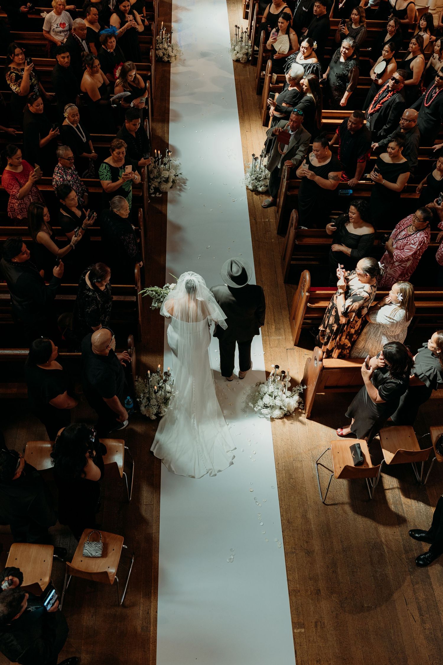 Wedding ceremony in progress viewed from above with guests seated in rows on wooden floors.