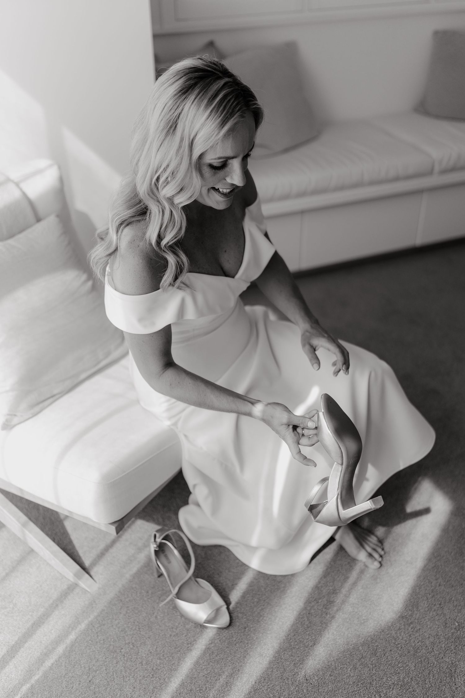 Black and white photos of bride putting on wedding shoes while sitting on white couch.
