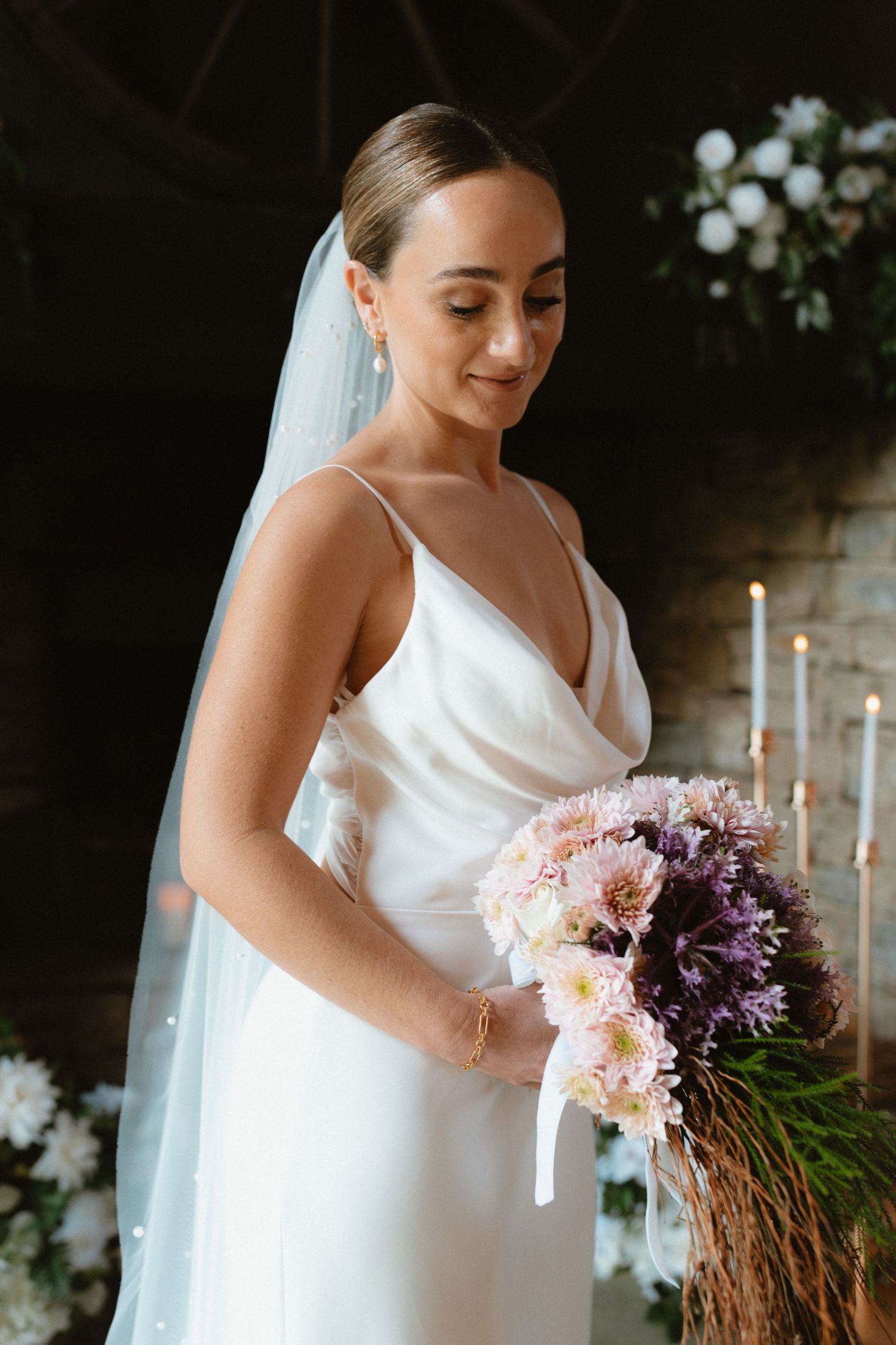 Bride in silk v-neck dress holds beautiful pink and purple bouquet.