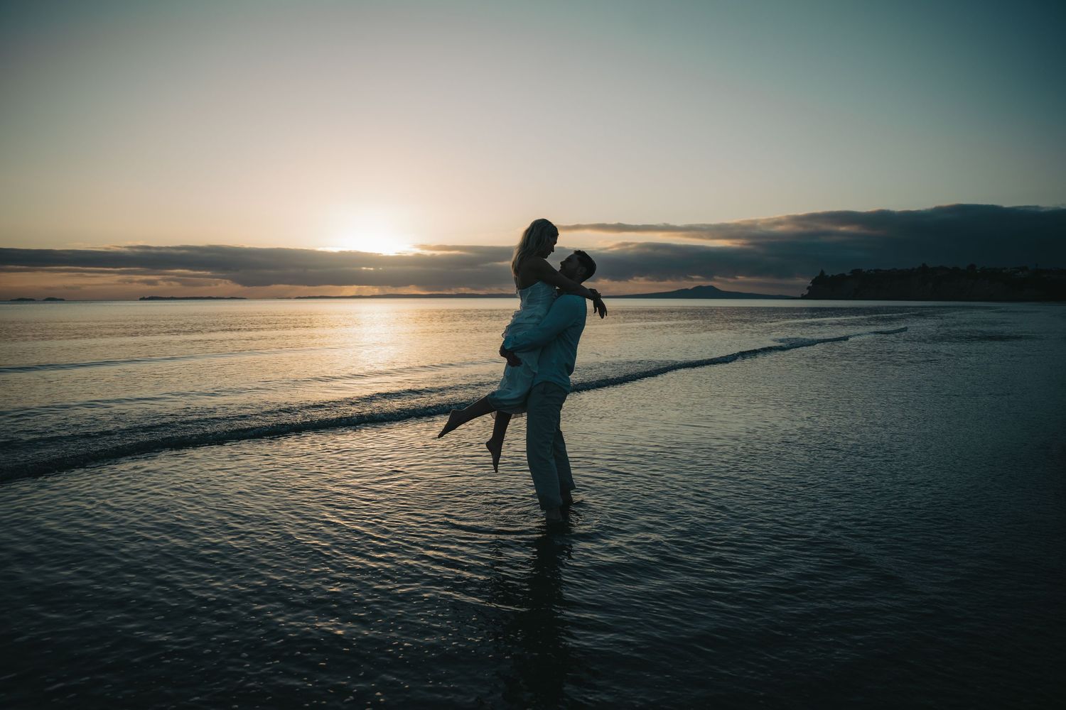 Silhouetted couple embracing in shallow ocean water during a romantic beach sunset.