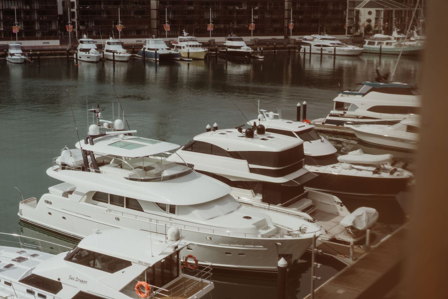 Luxury yachts and boats docked in a marina with white vessels of varying sizes moored side by side.