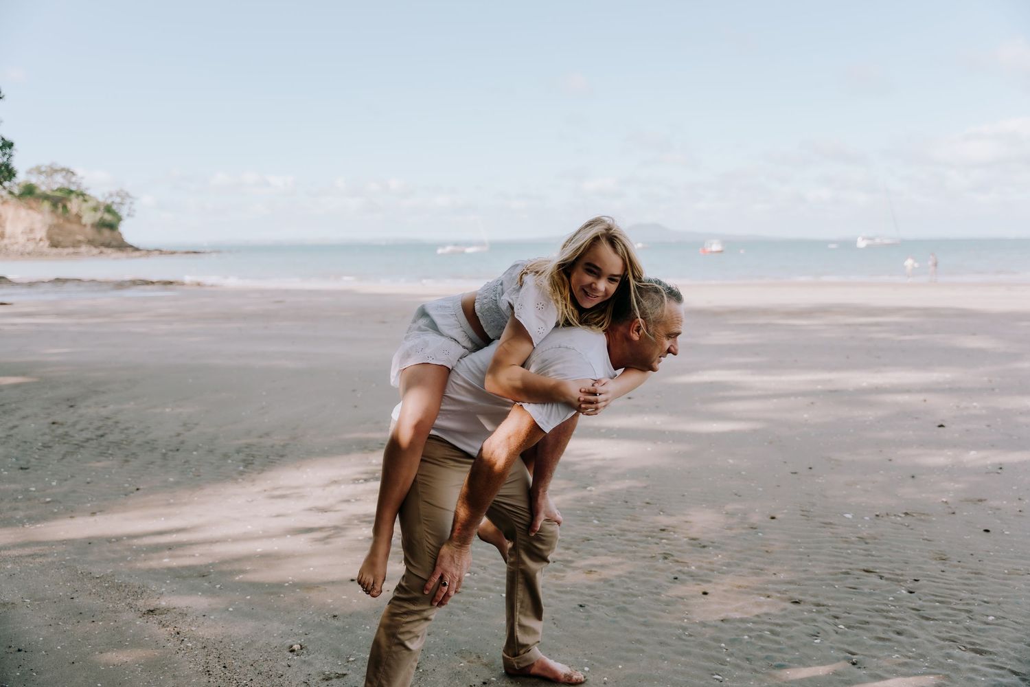 A playful moment shared between two people on a sandy beach with ocean and cliffs in the background.