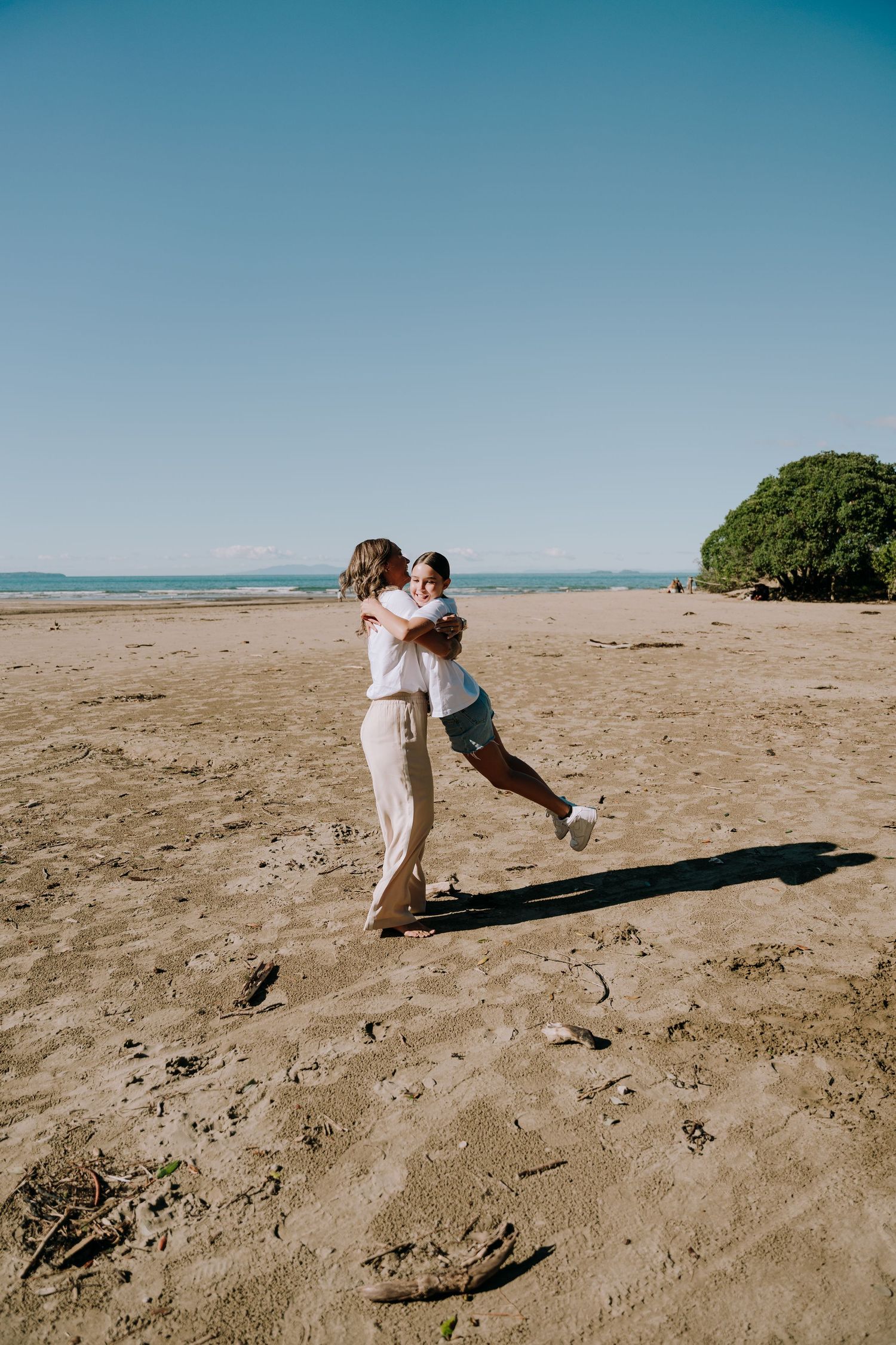A couple dances and dips romantically on a sandy beach with blue sky and green foliage in the background.