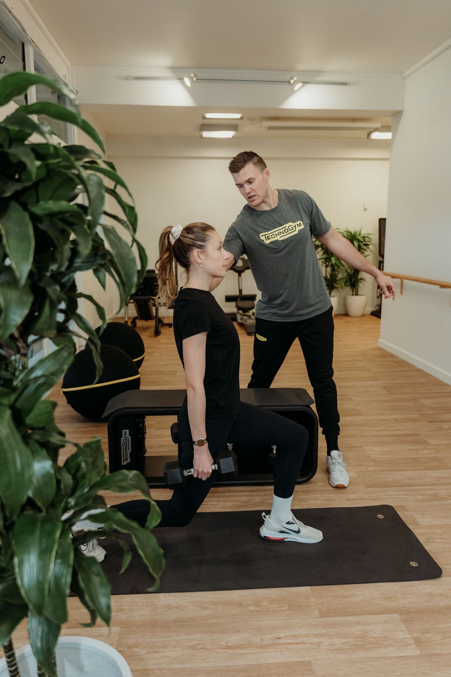 Personal trainer coaching a woman doing dumbbell exercises on a bench in a modern gym studio.