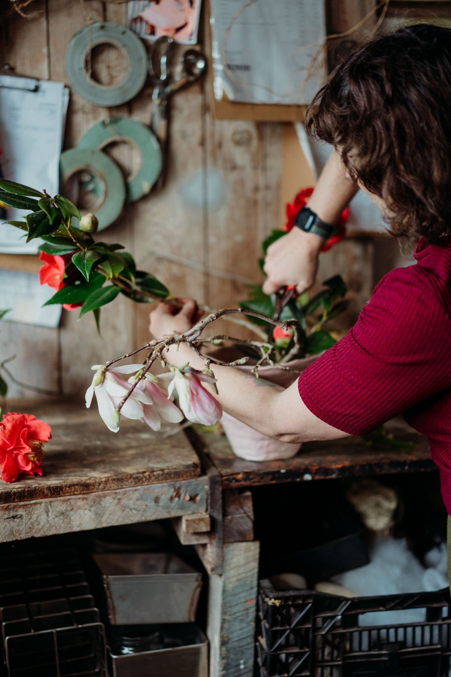 Florist arranging red and white flowers on a rustic wooden workbench in a floral shop.