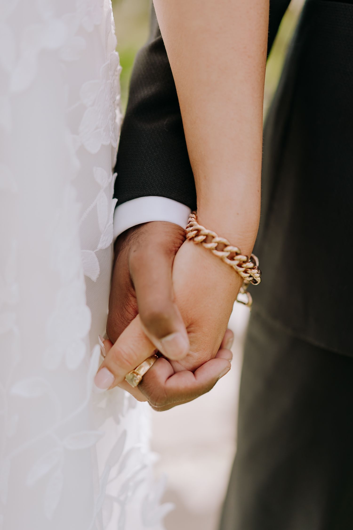 Close-up view of a bride and groom holding hands showing their wedding rings and jewelry.