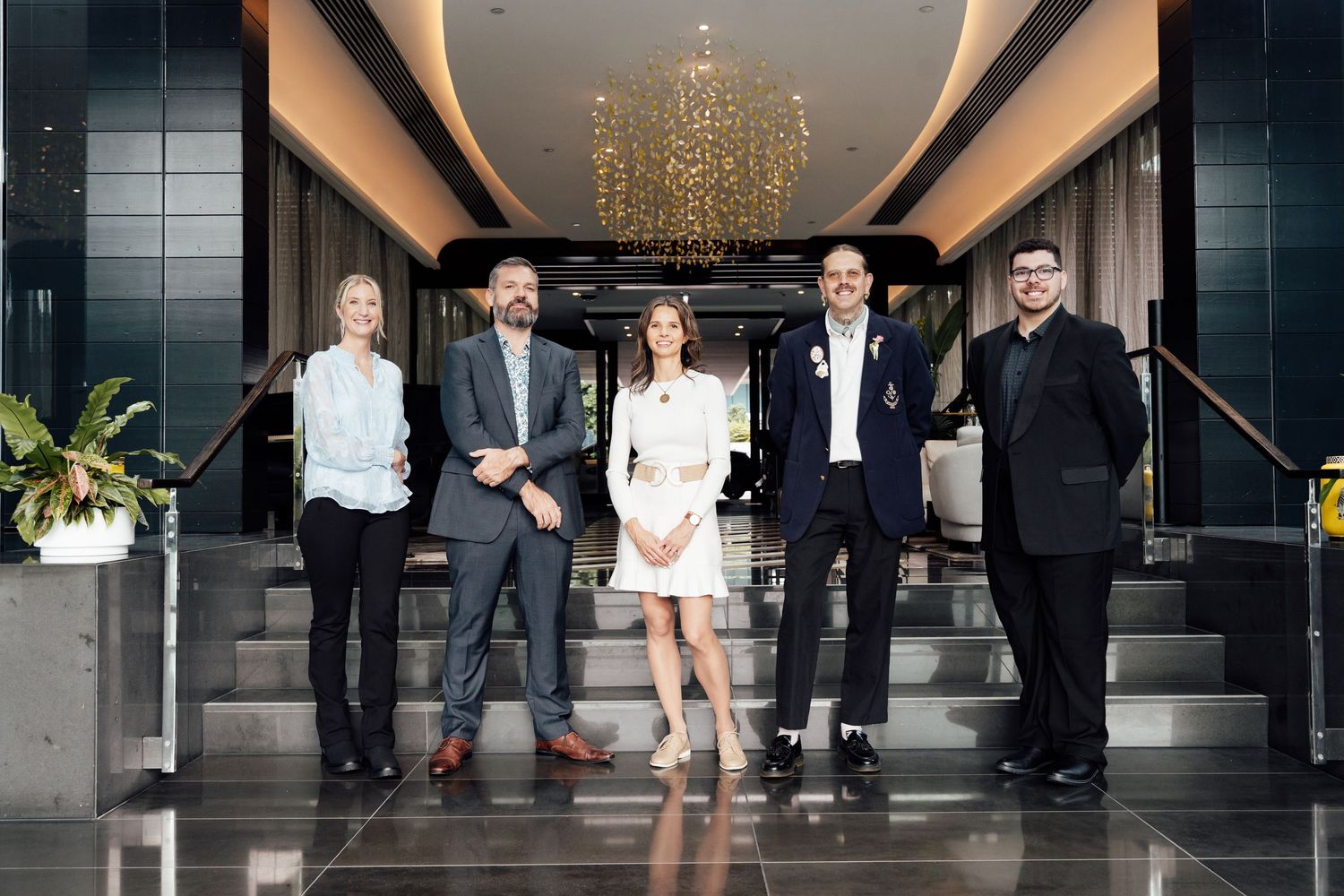 Five professionals pose together in a modern hotel lobby with chandelier lighting and elegant decor.