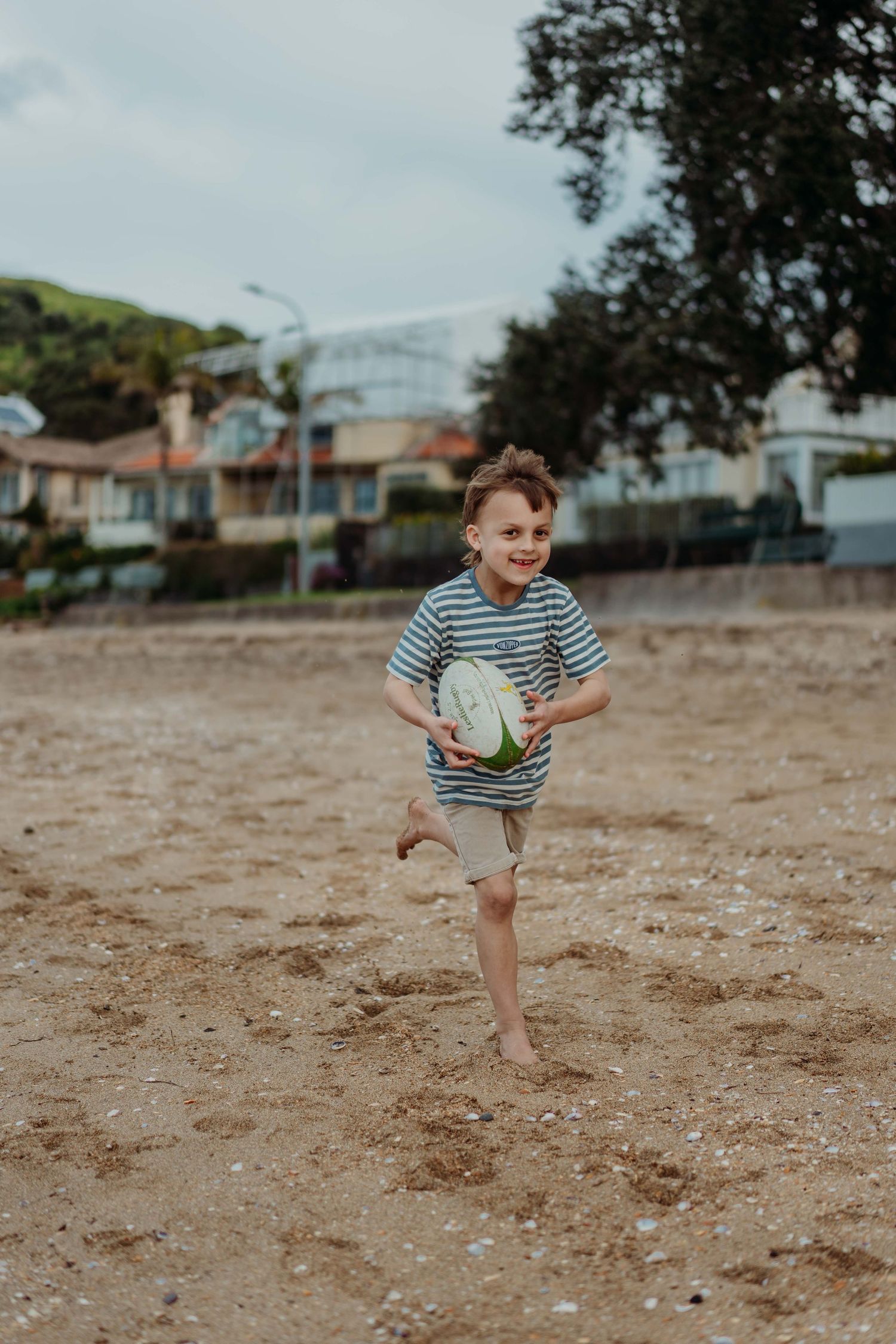 A young child runs and plays barefoot on sandy ground near houses on a sunny day.