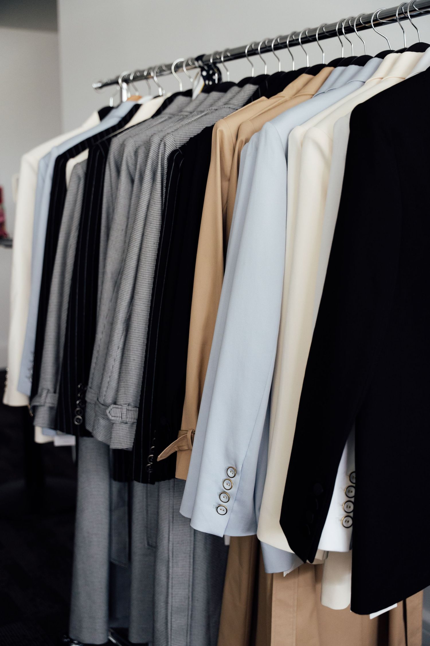 A row of elegant suits and blazers in neutral tones hanging on a clothing rack in a boutique store.