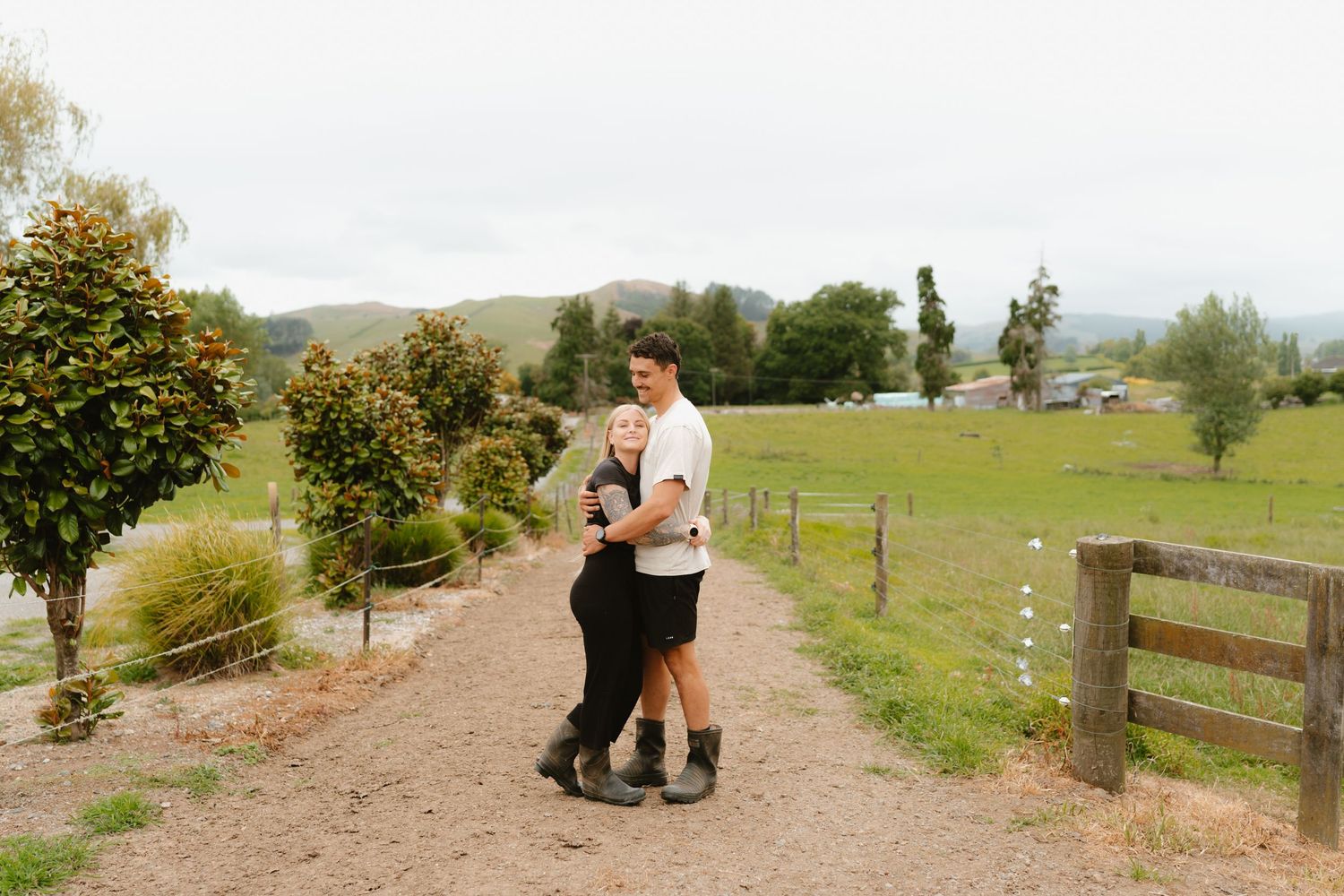 A couple embracing on a rustic dirt path lined with citrus trees and wooden fencing.