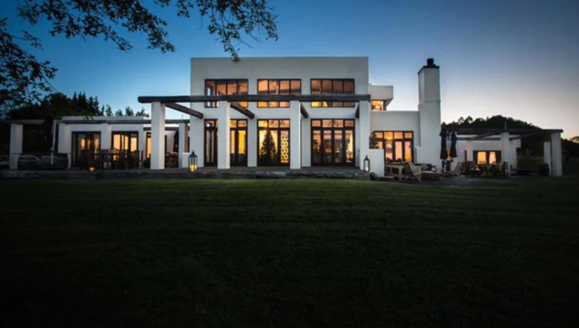 Modern luxury mansion illuminated at dusk with large windows and contemporary architectural design.