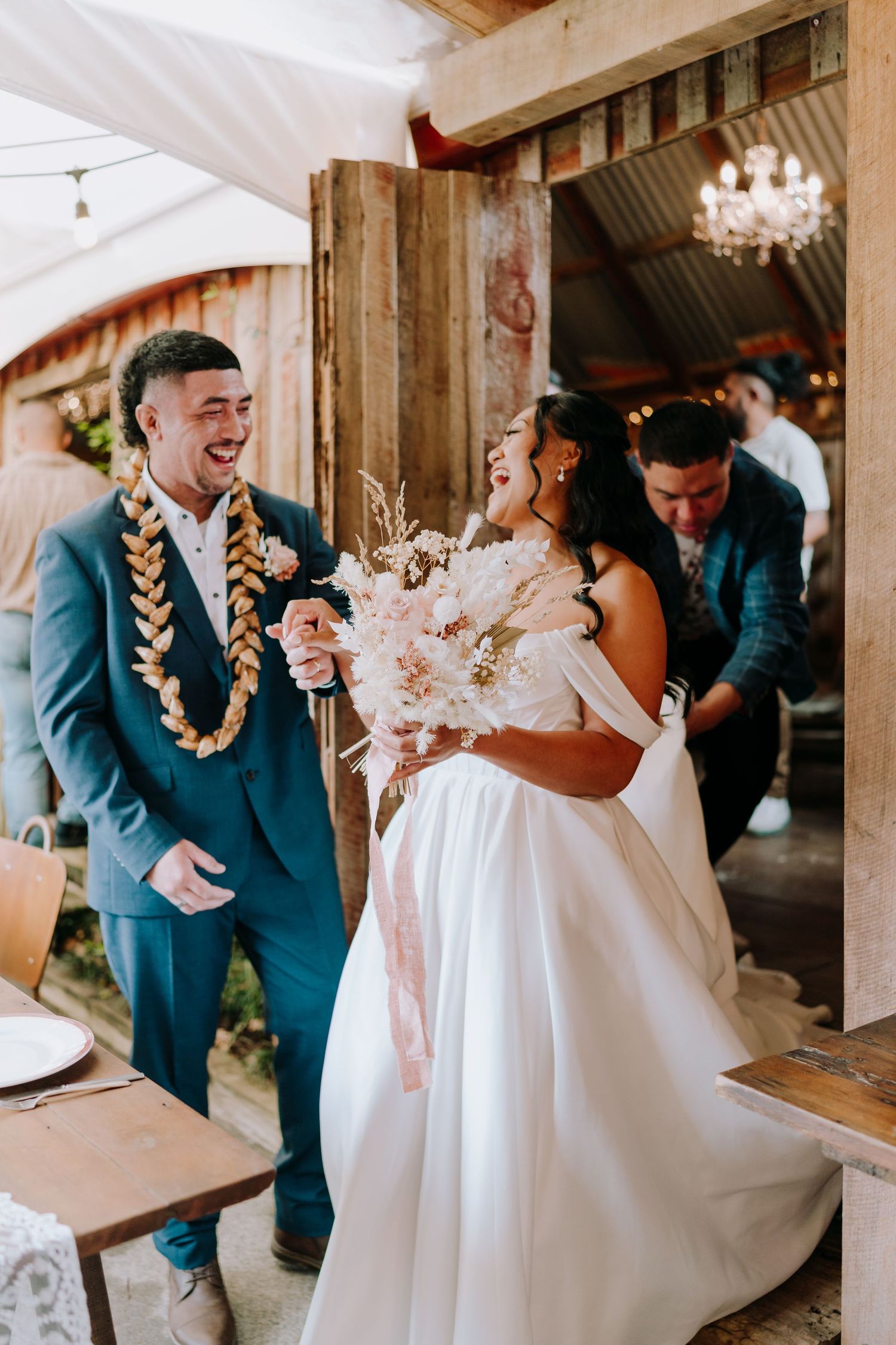 Newlyweds share joyful moment in rustic venue with traditional Hawaiian leis.