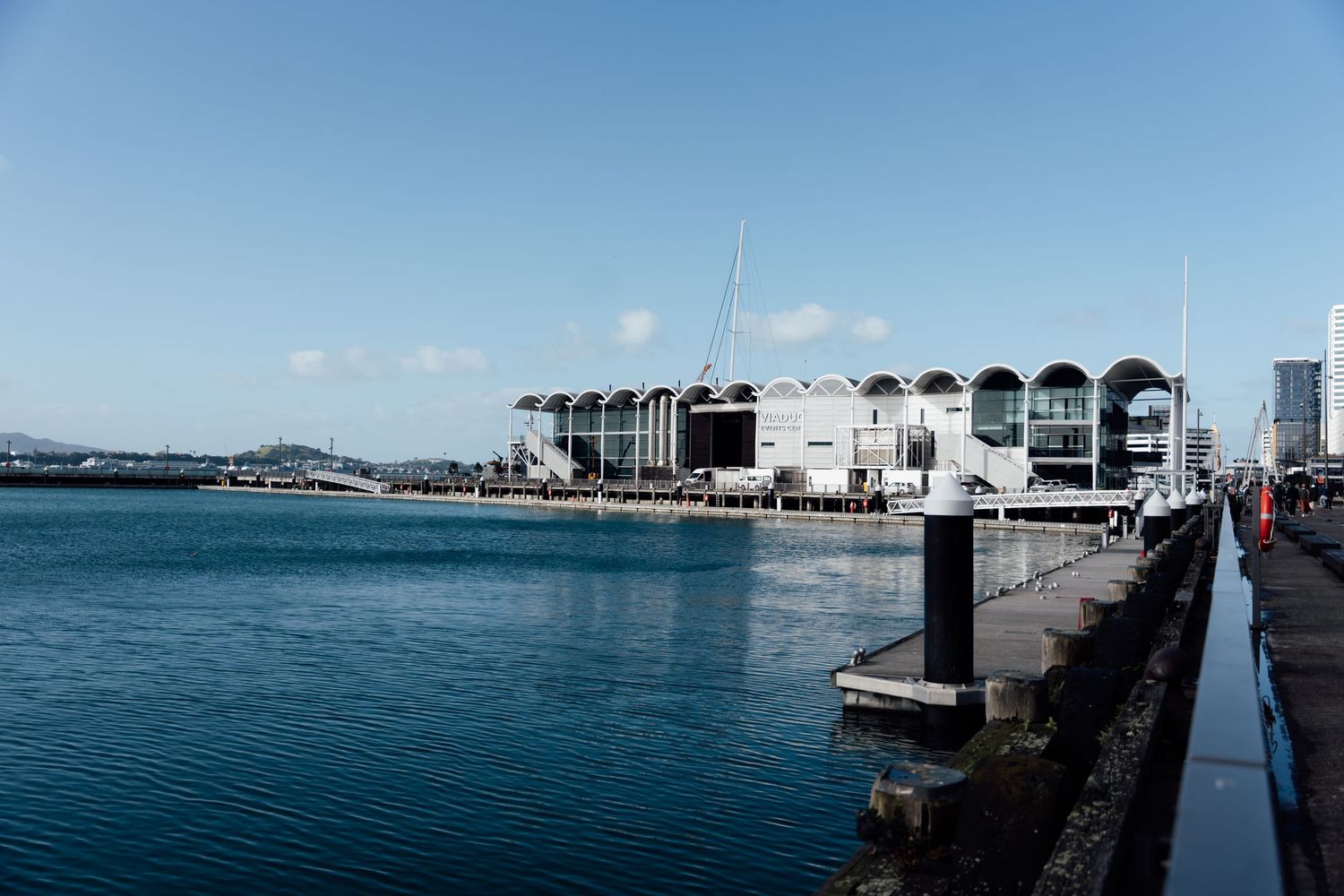 Waterfront view of a modern curved building along Auckland's Viaduct Harbour on a clear sunny day.