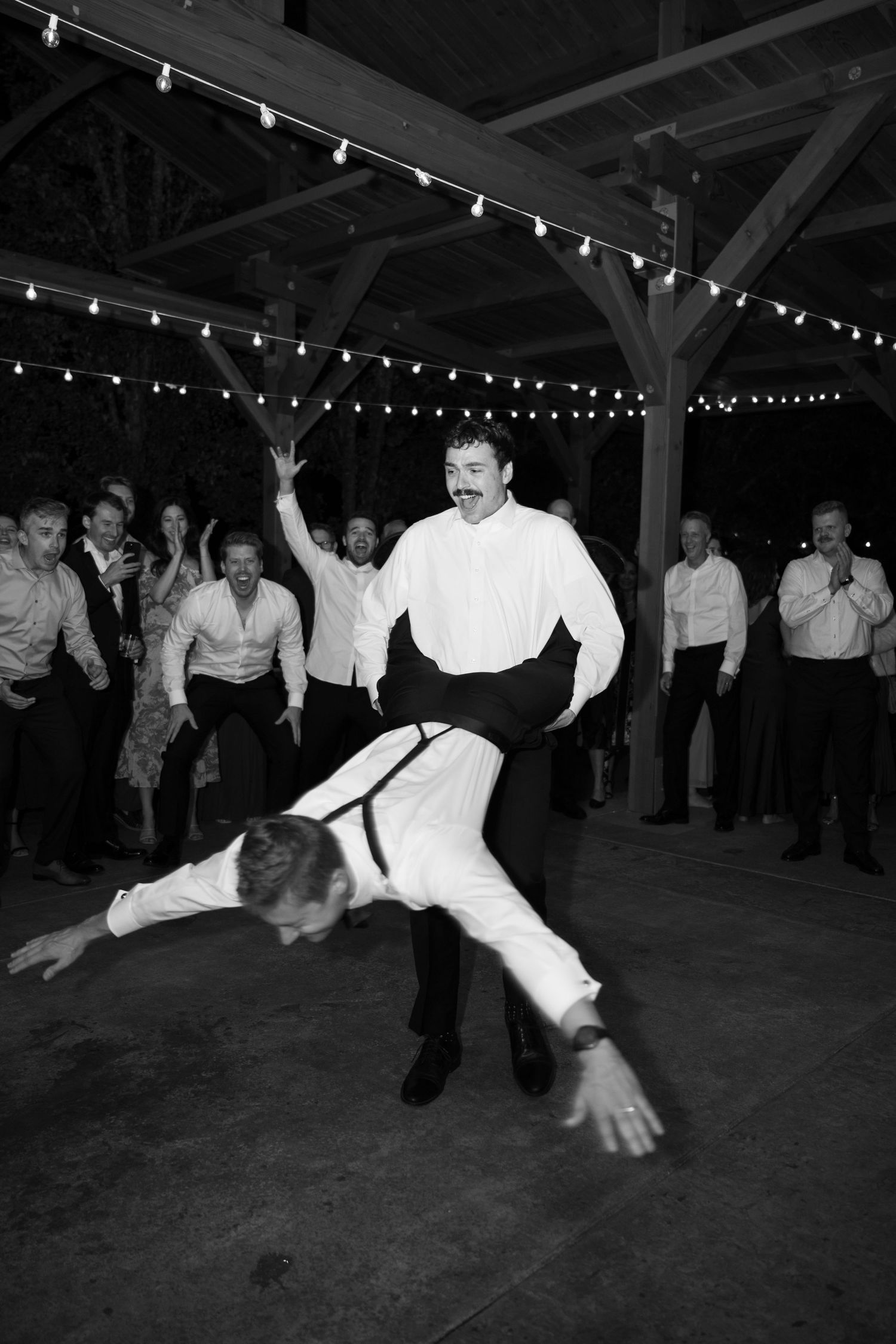Black and white photo of energetic wedding guests performing acrobatic dance moves at reception.