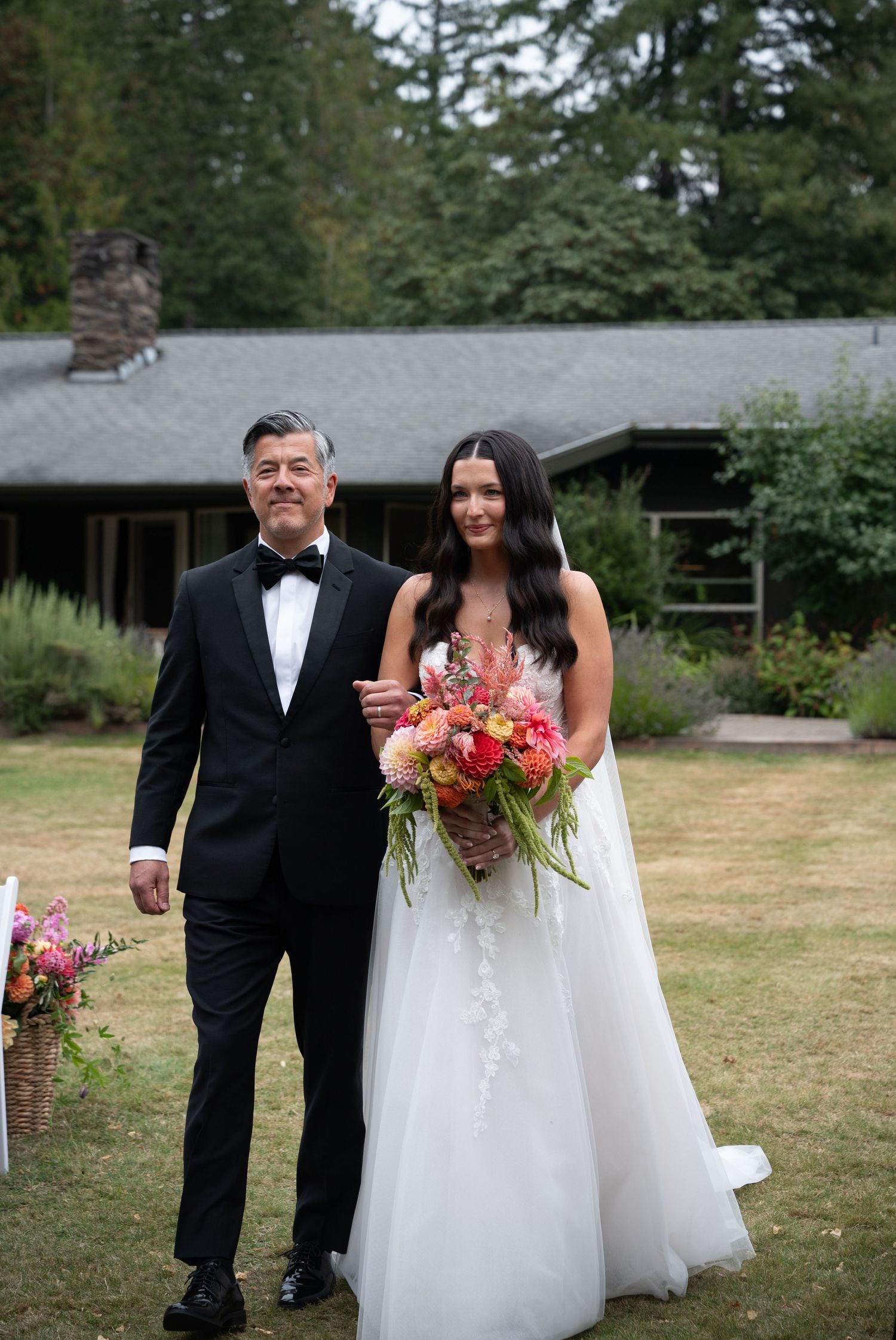 Bride in white gown holding colorful bouquet walking with man in tuxedo.