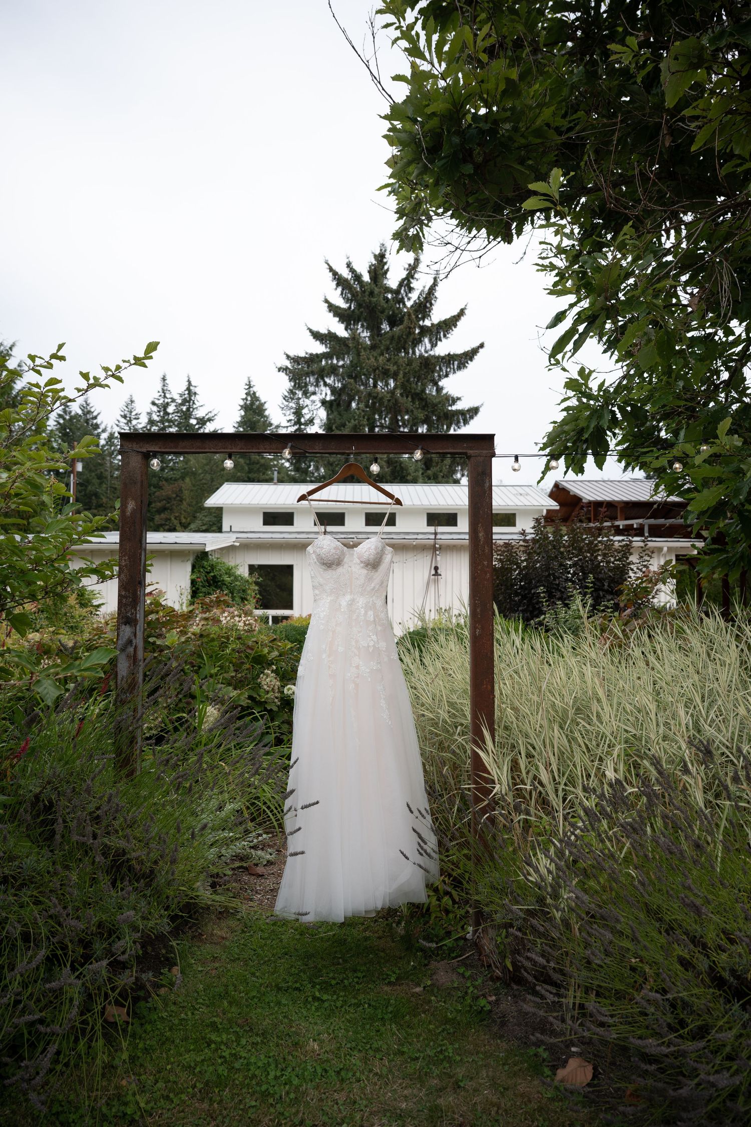 Wedding dress hanging on wooden frame arch surrounded by lush garden greenery.