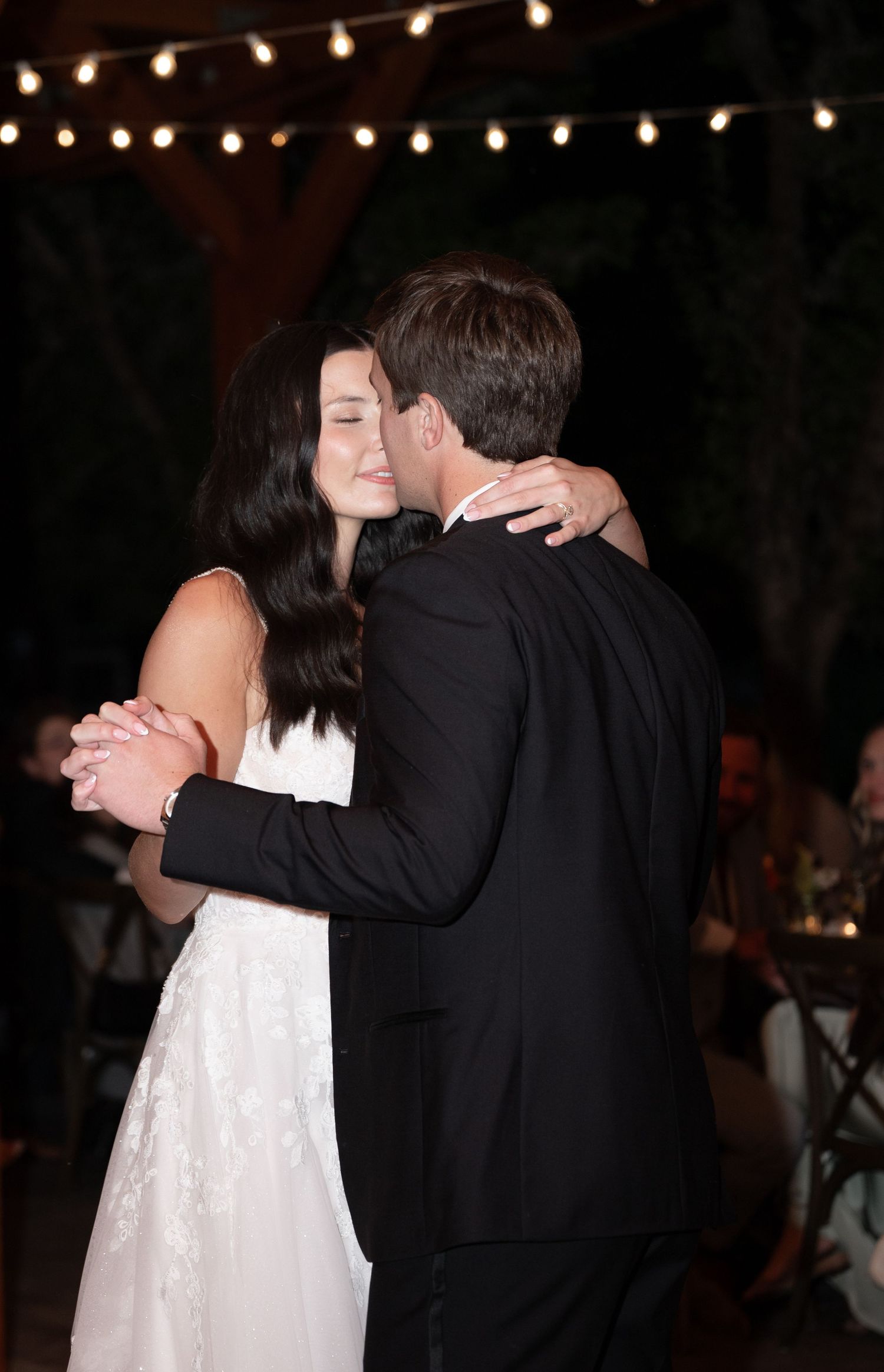 Bride and groom sharing an intimate first dance under string lights at their evening wedding reception.