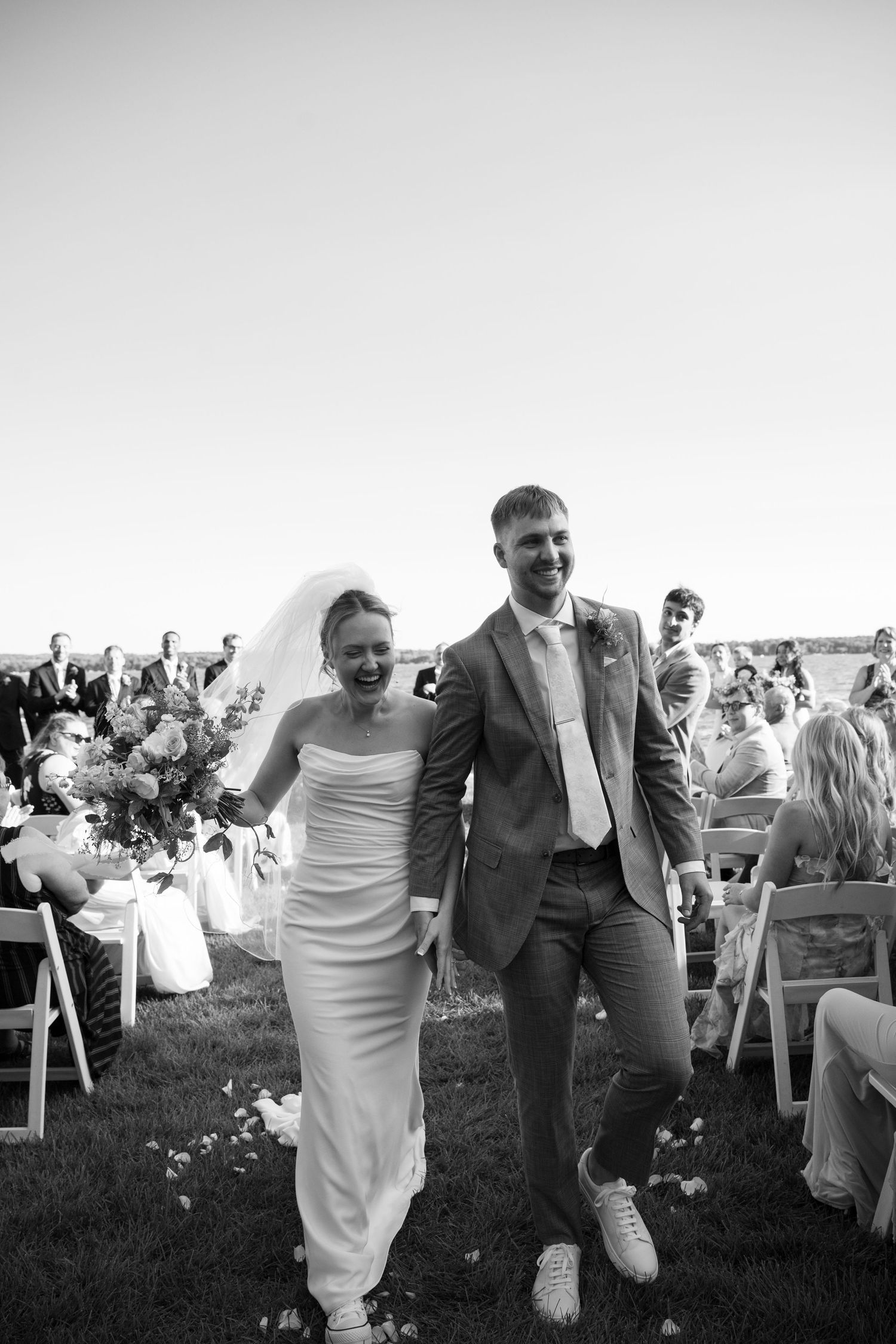 Black and white photo of a joyful bride and groom walking back down the aisle at an outdoor wedding ceremony.