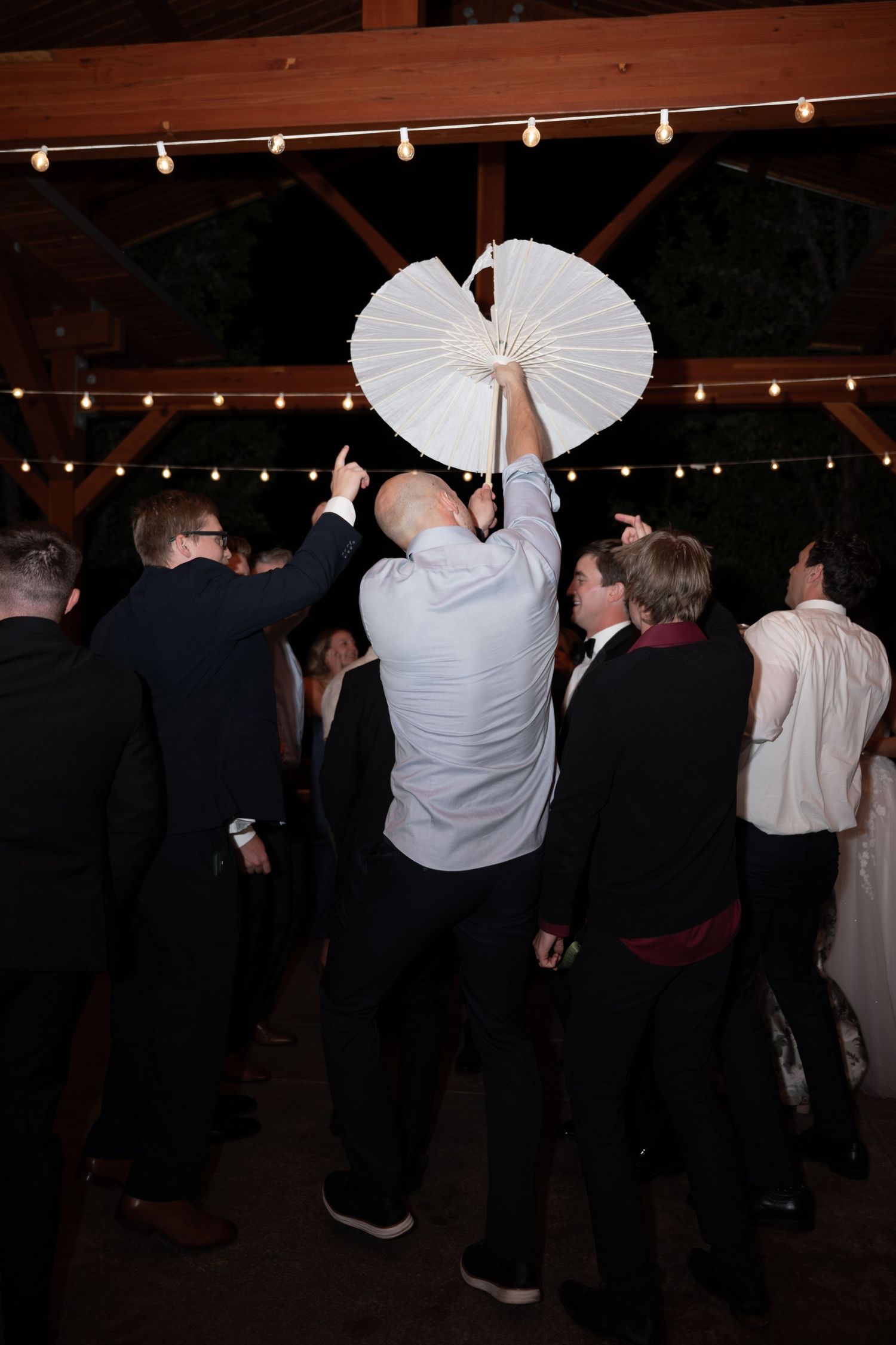Wedding guest dances holding white parasol under string lights at outdoor reception venue.