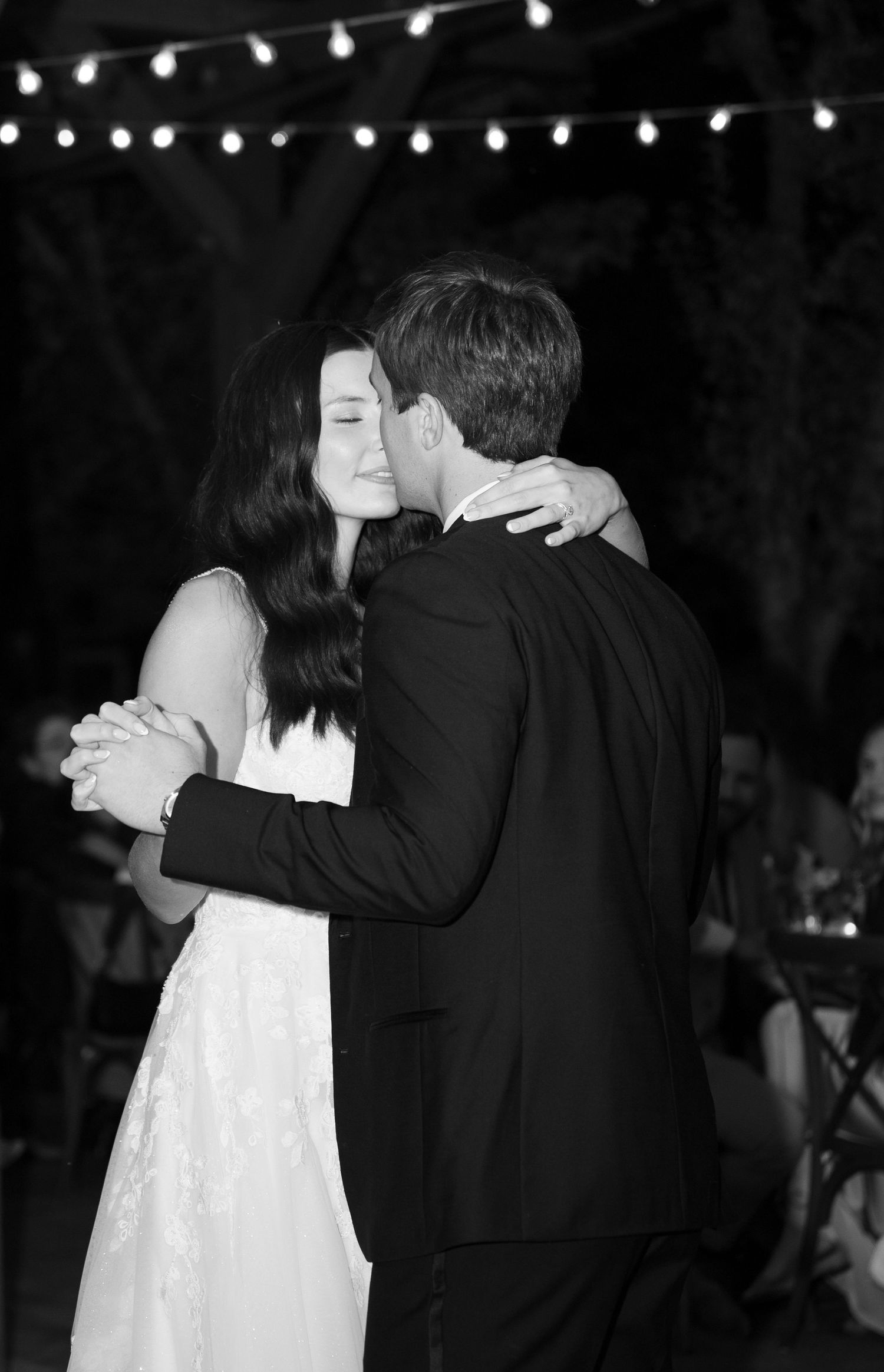 Bride and groom share an intimate first dance embrace under string lights at their wedding reception.