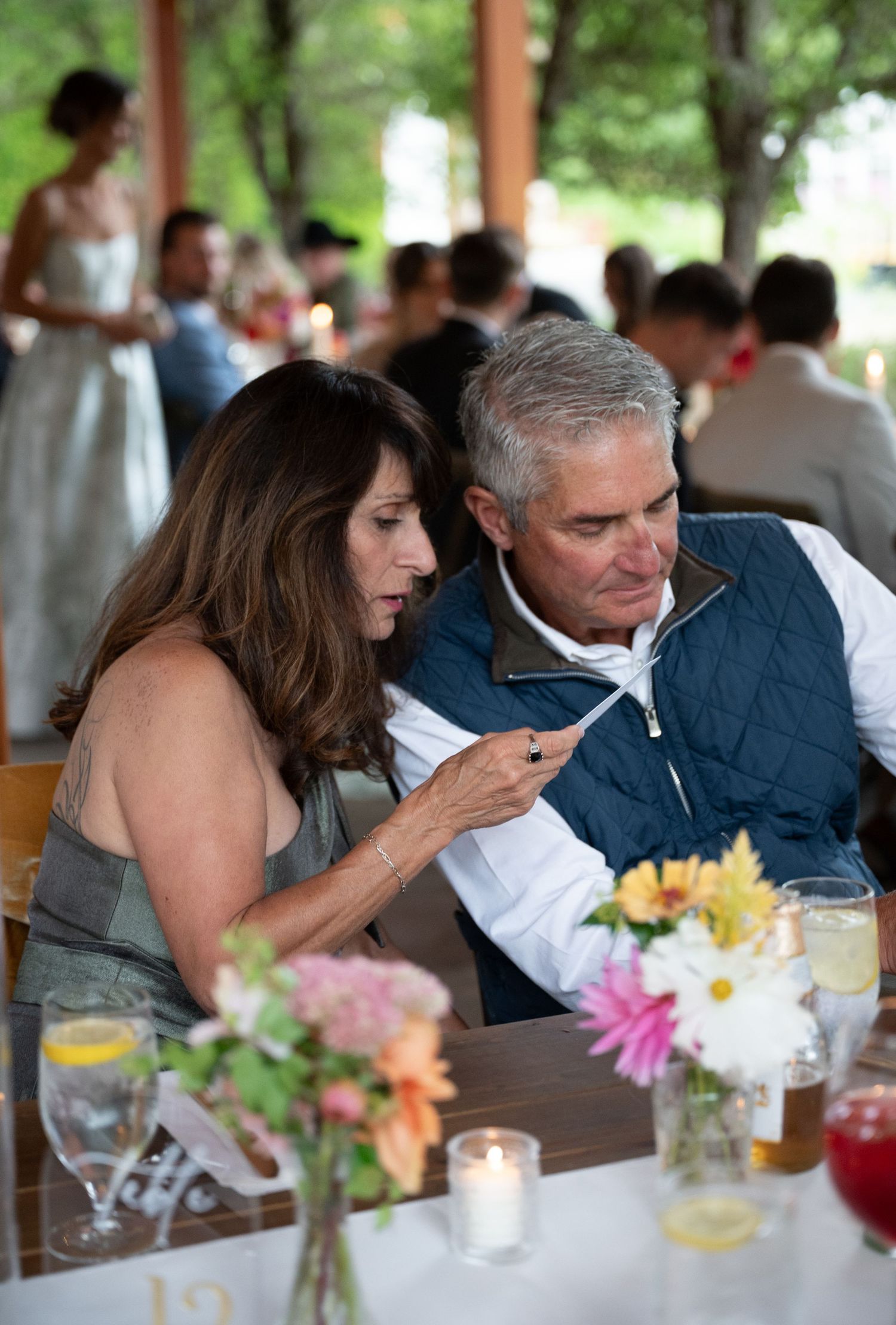 Couple at wedding reception table looking at phone together surrounded by floral centerpieces and candles.
