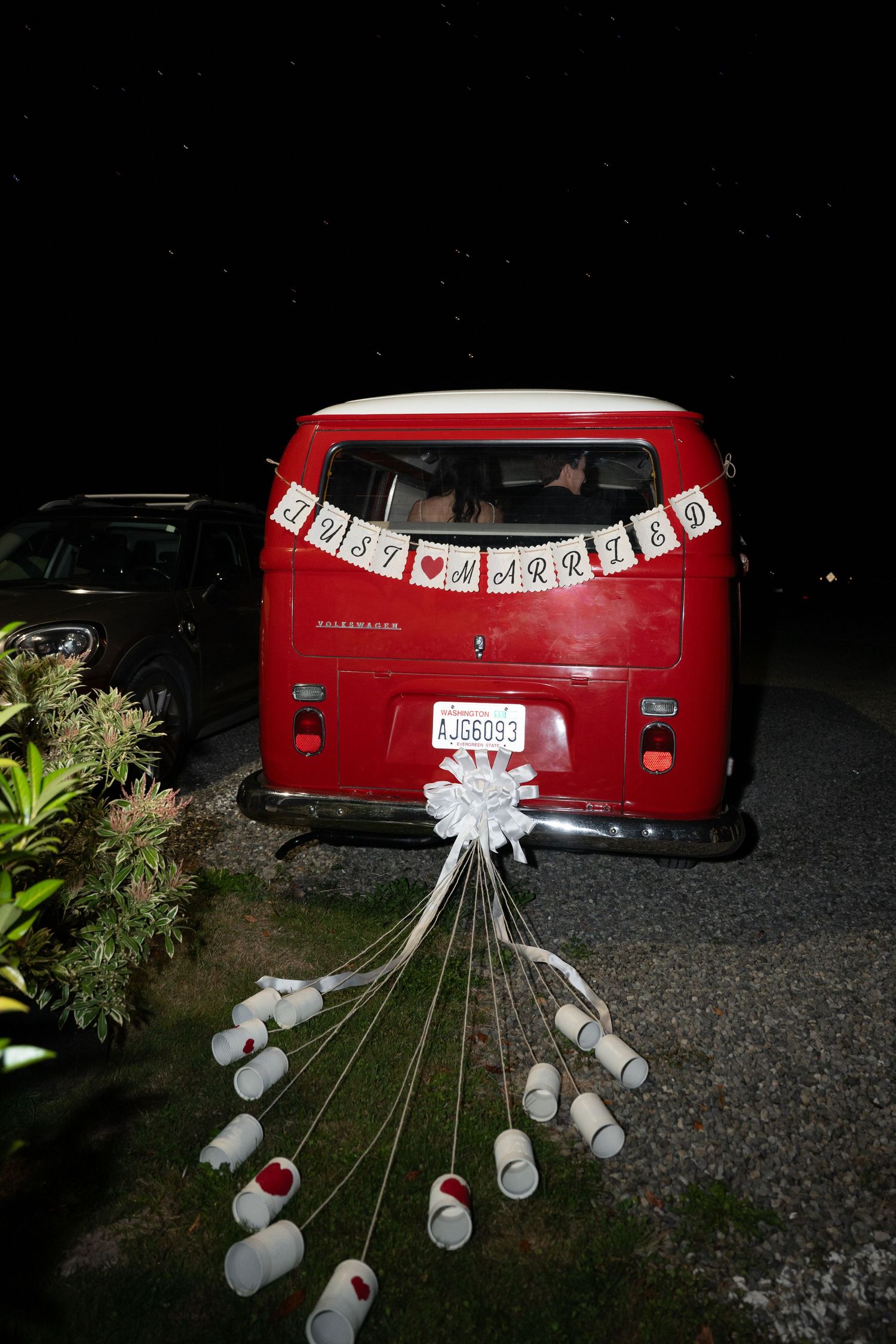 Vintage red VW van decorated with Just Married banner and tin cans at night.
