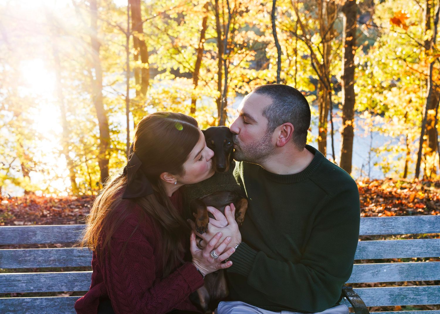 Couple in autumn attire sharing a romantic moment on a wooden bench surrounded by fall foliage.