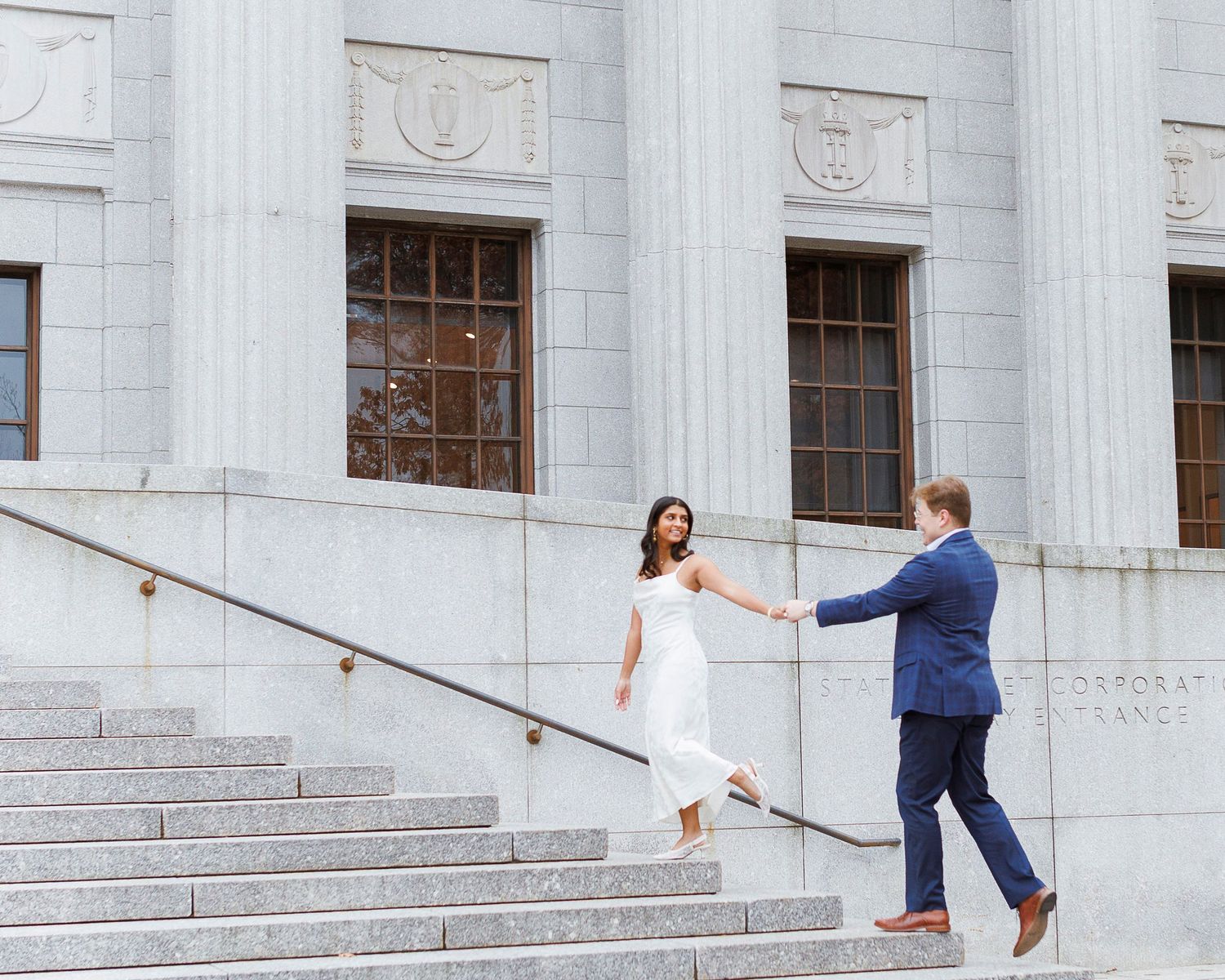 A couple dances on the steps of a grand stone building with classical columns and architecture.