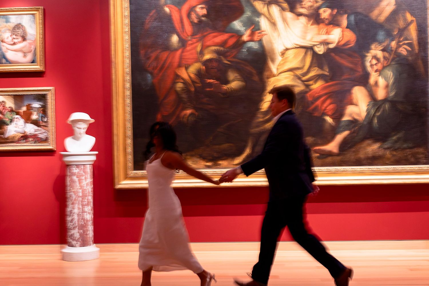 Two dancers perform a tango dance in an art gallery with red walls displaying classical paintings.