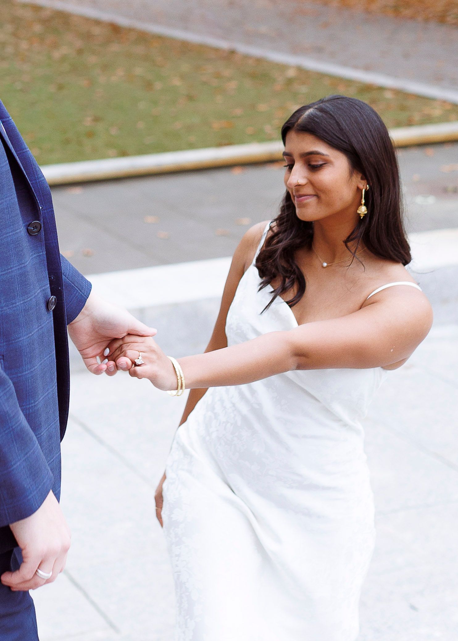 A couple in formal wedding attire exchange rings during an outdoor ceremony.