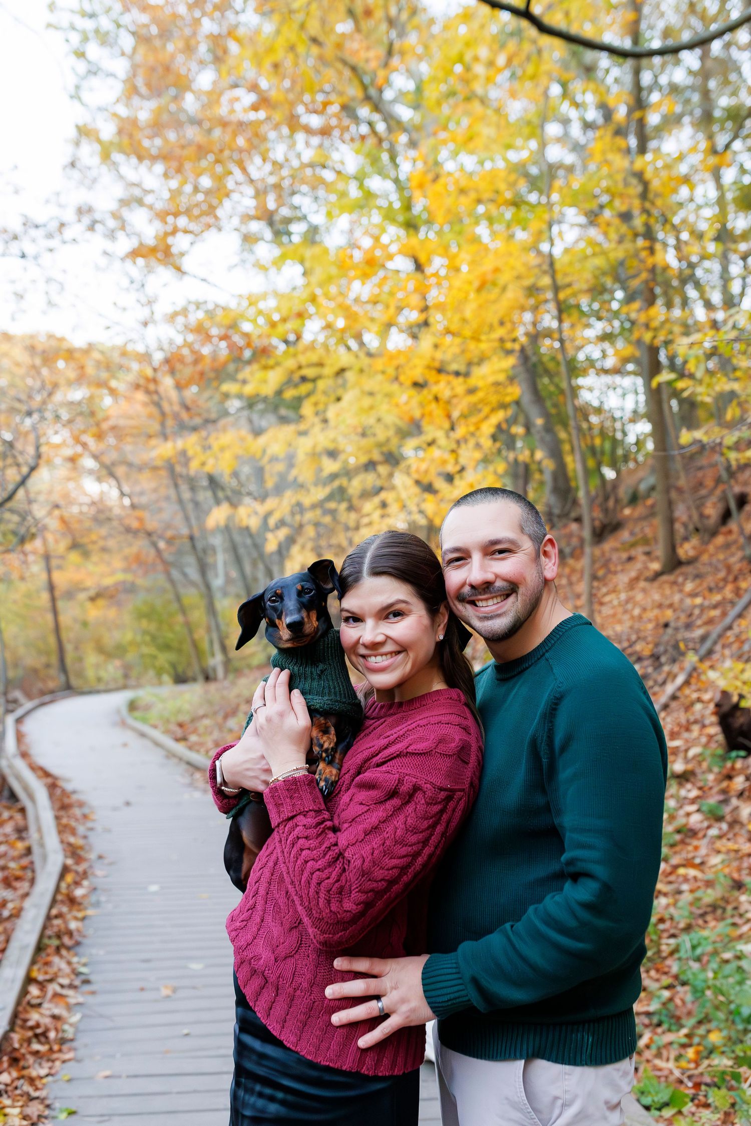 A couple enjoys an autumn stroll on a wooden boardwalk surrounded by vibrant fall foliage.
