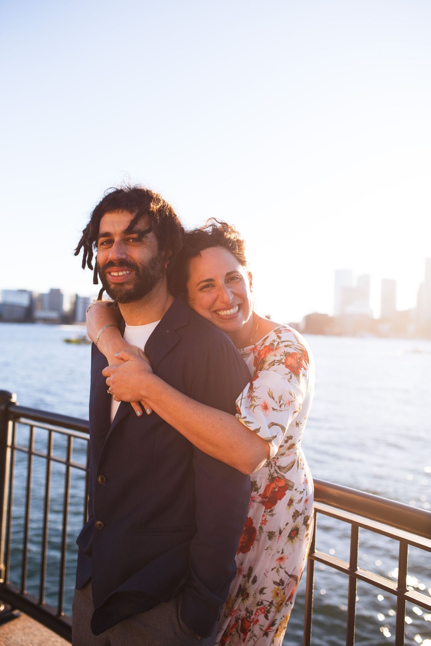 Couple shares intimate moment on waterfront pier during golden hour with harbor views.
