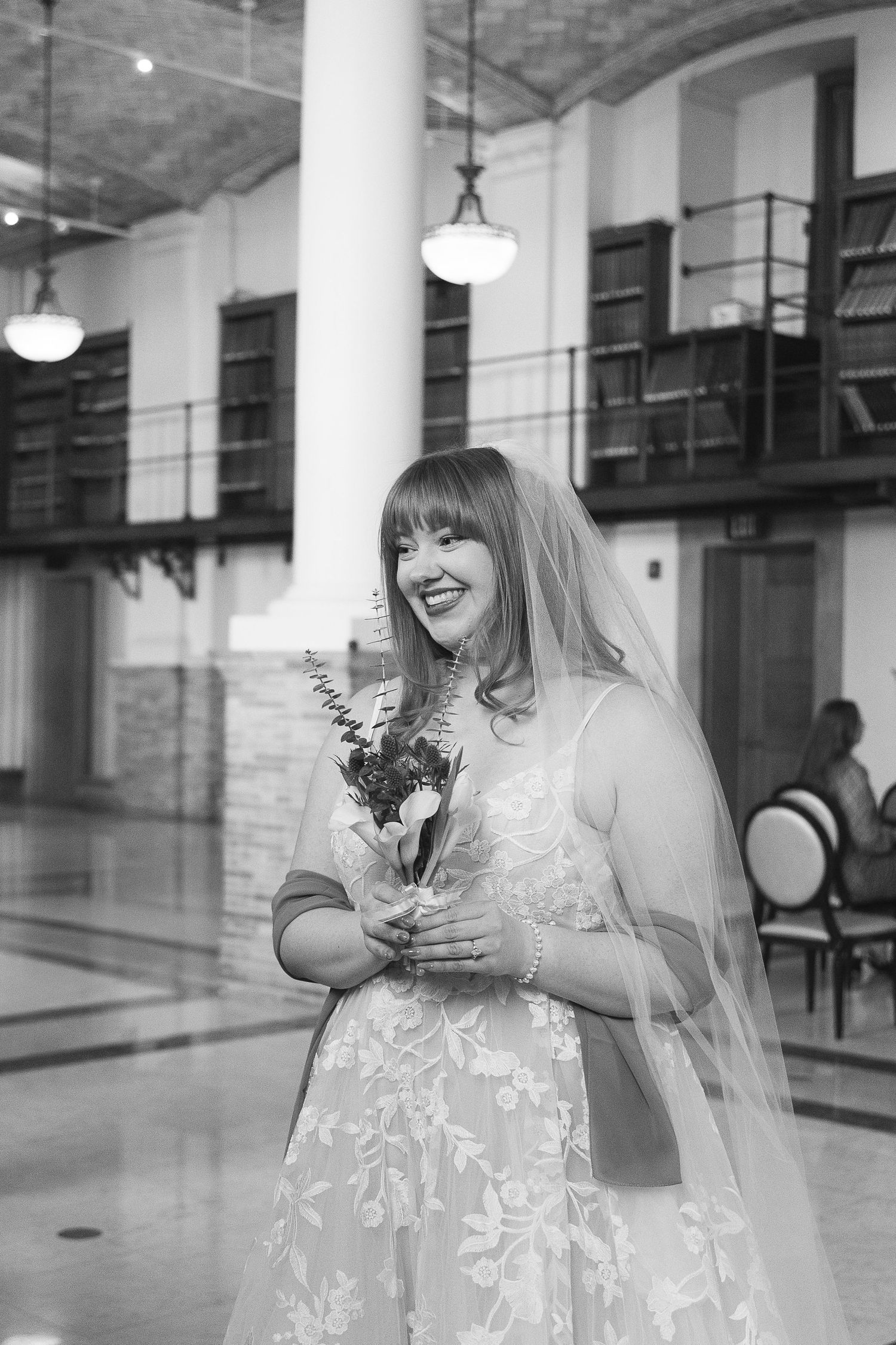A joyful moment captured in black and white inside an elegant venue with tall columns and pendant lights.