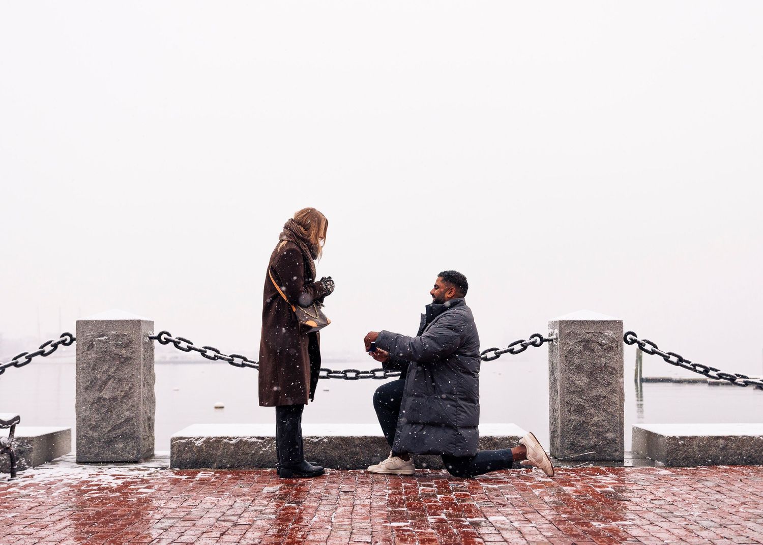 Two figures sit on a stone ledge connected by chain links during a rainy day.