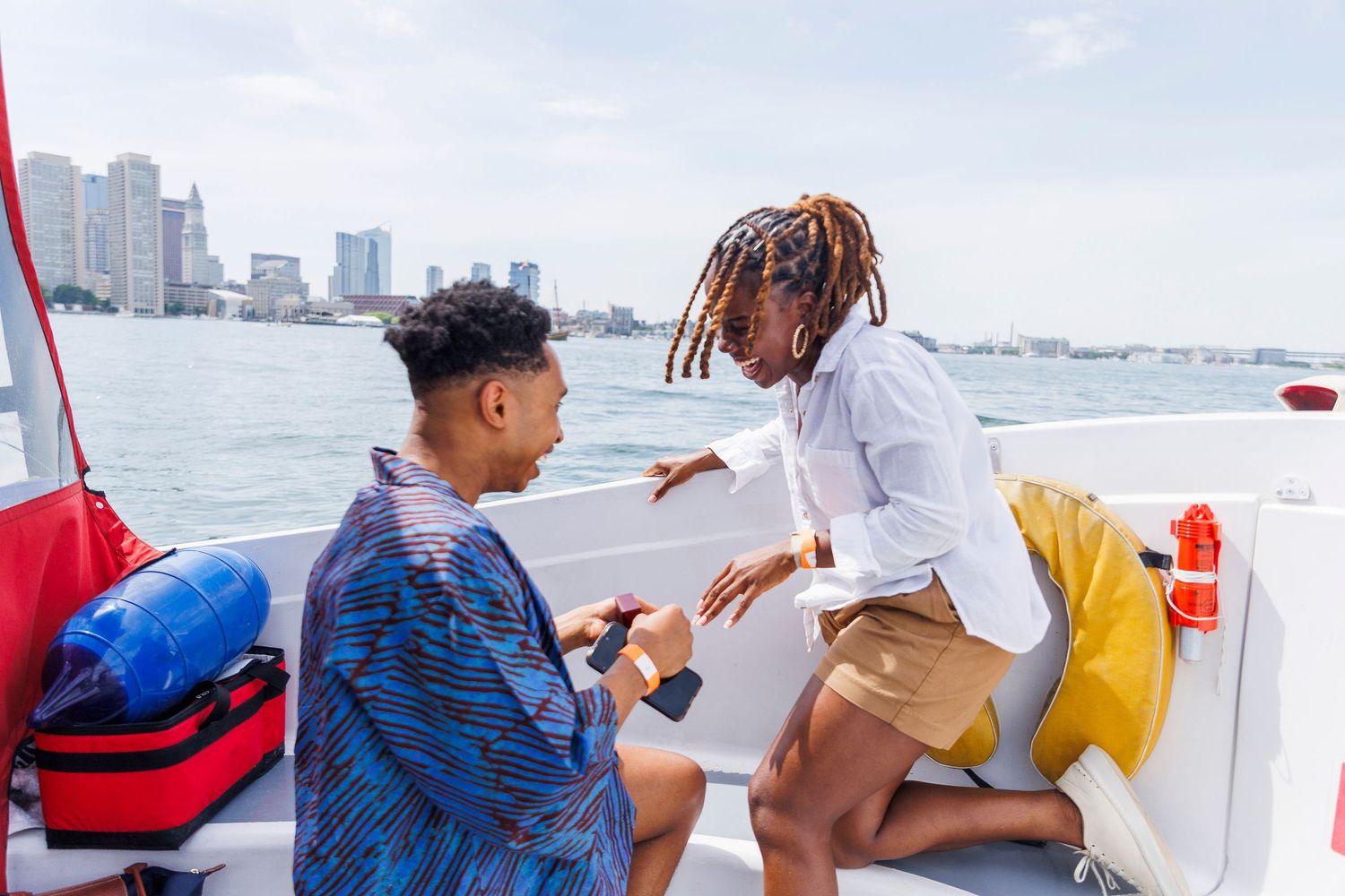 Couple sharing a romantic moment on a boat with city skyline views on a sunny day.