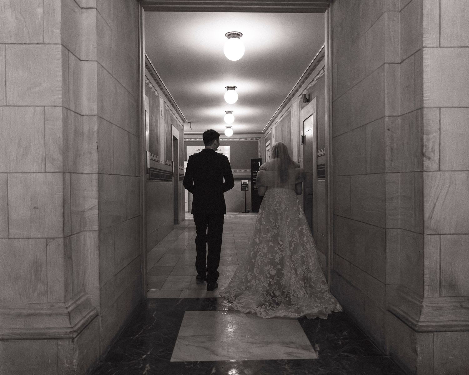 A dimly lit marble corridor with repeating columns and recessed lighting creates an eerie institutional atmosphere.