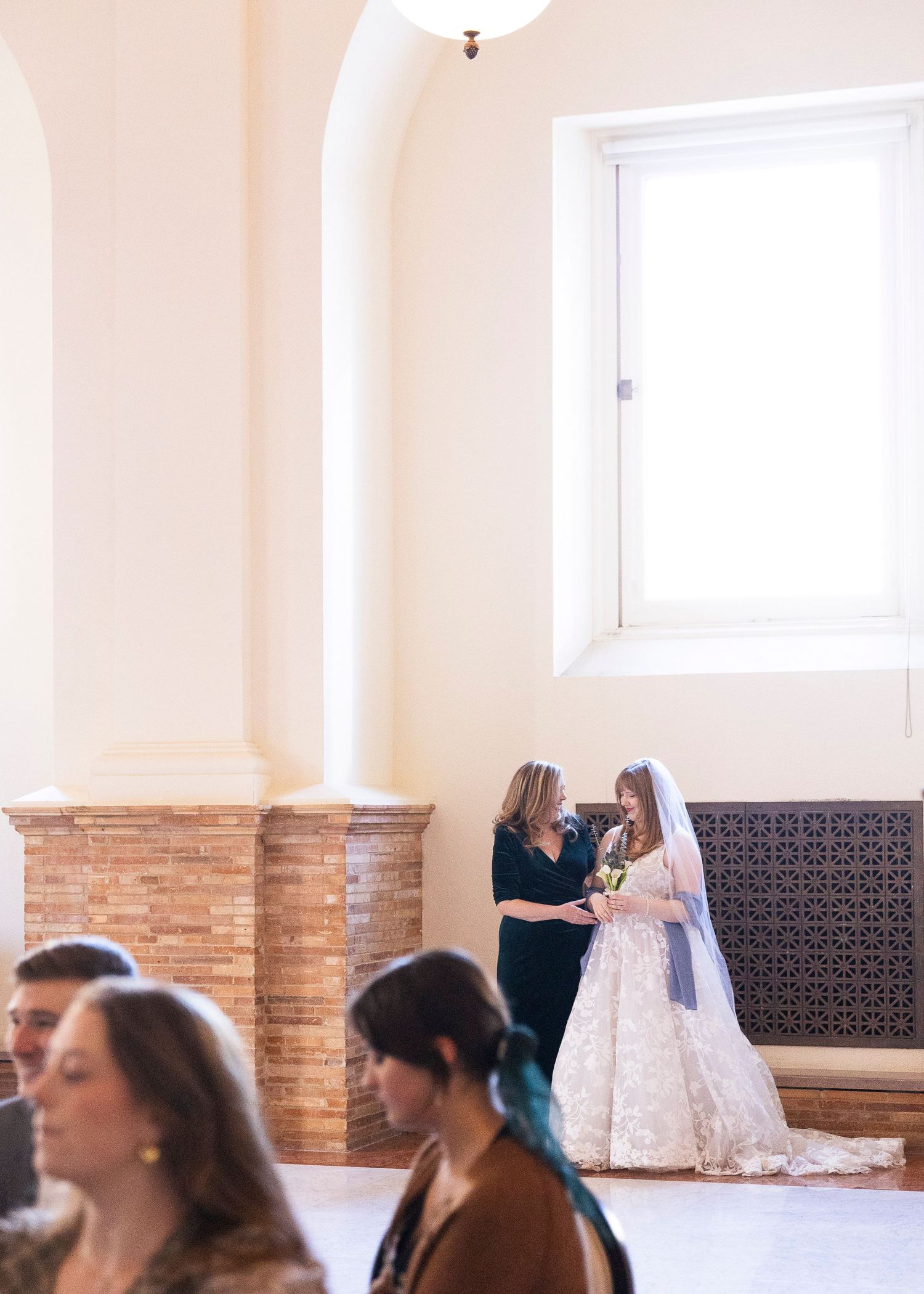A wedding ceremony moment in a bright room with exposed brick columns and a window.