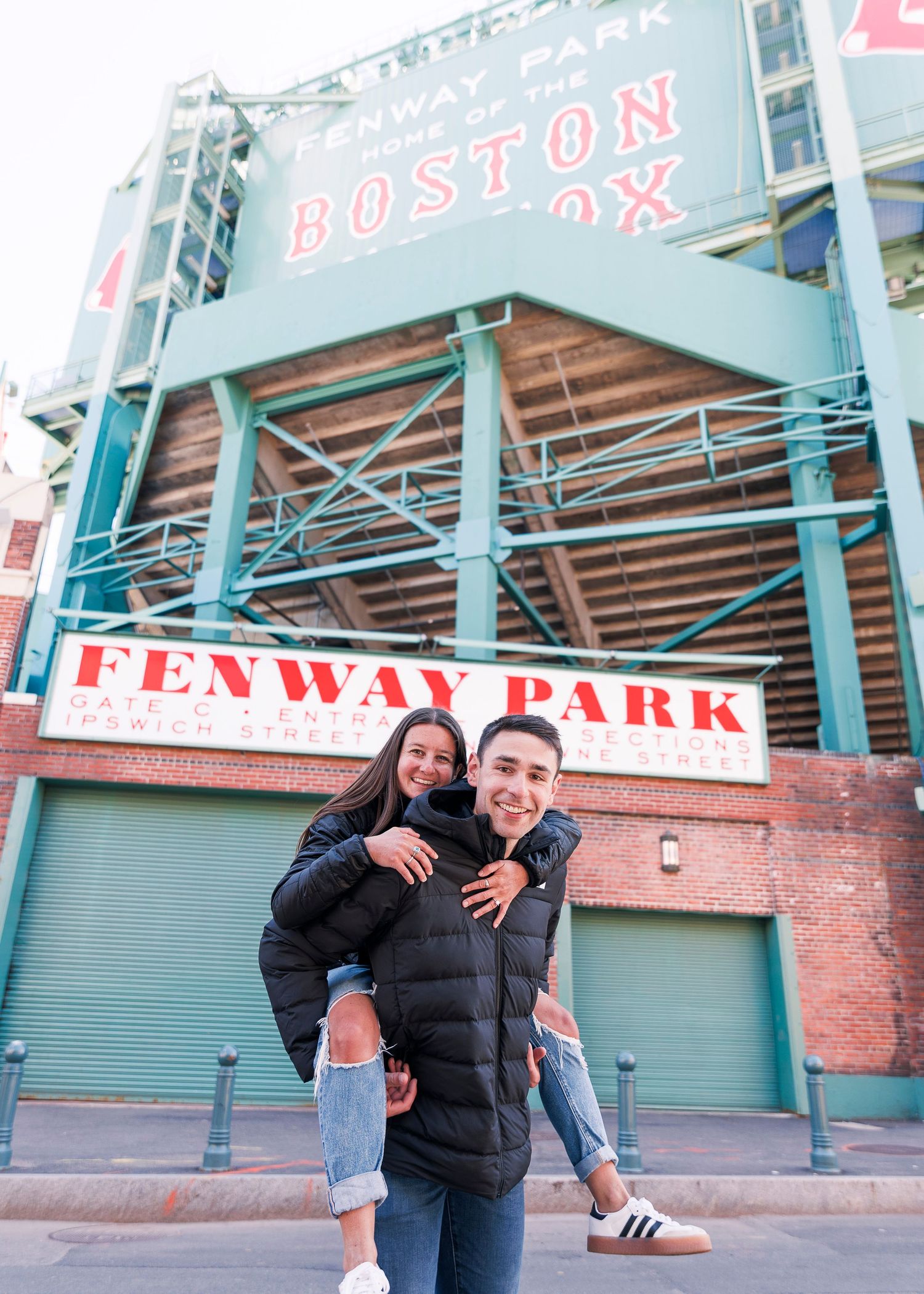 Couple posing and smiling in front of Fenway Park stadium sign in Boston, MA.
